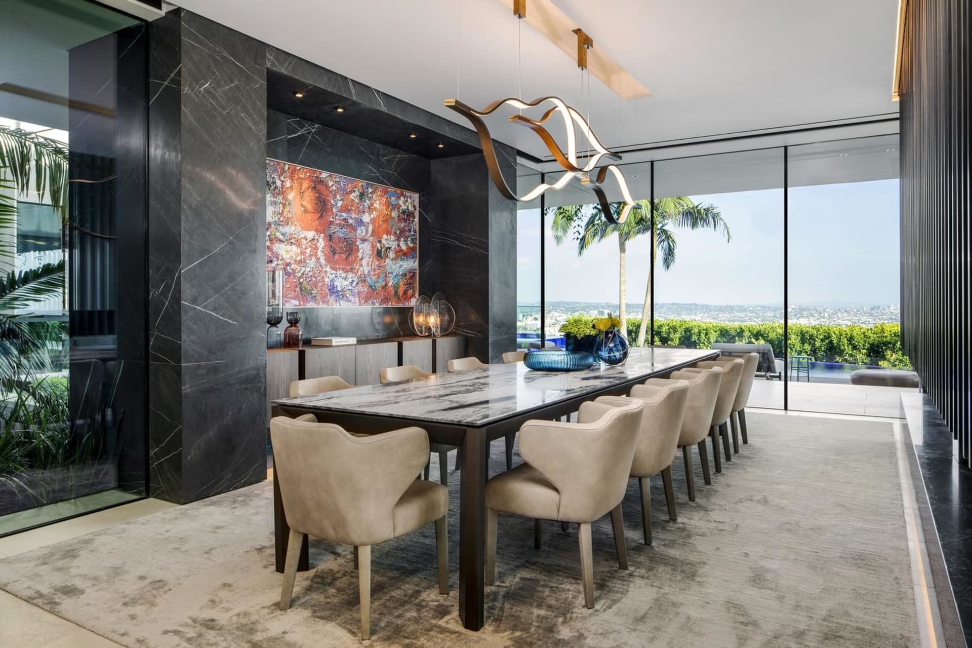 A modern dining room featuring a marble table, upholstered chairs, and a contemporary light fixture.