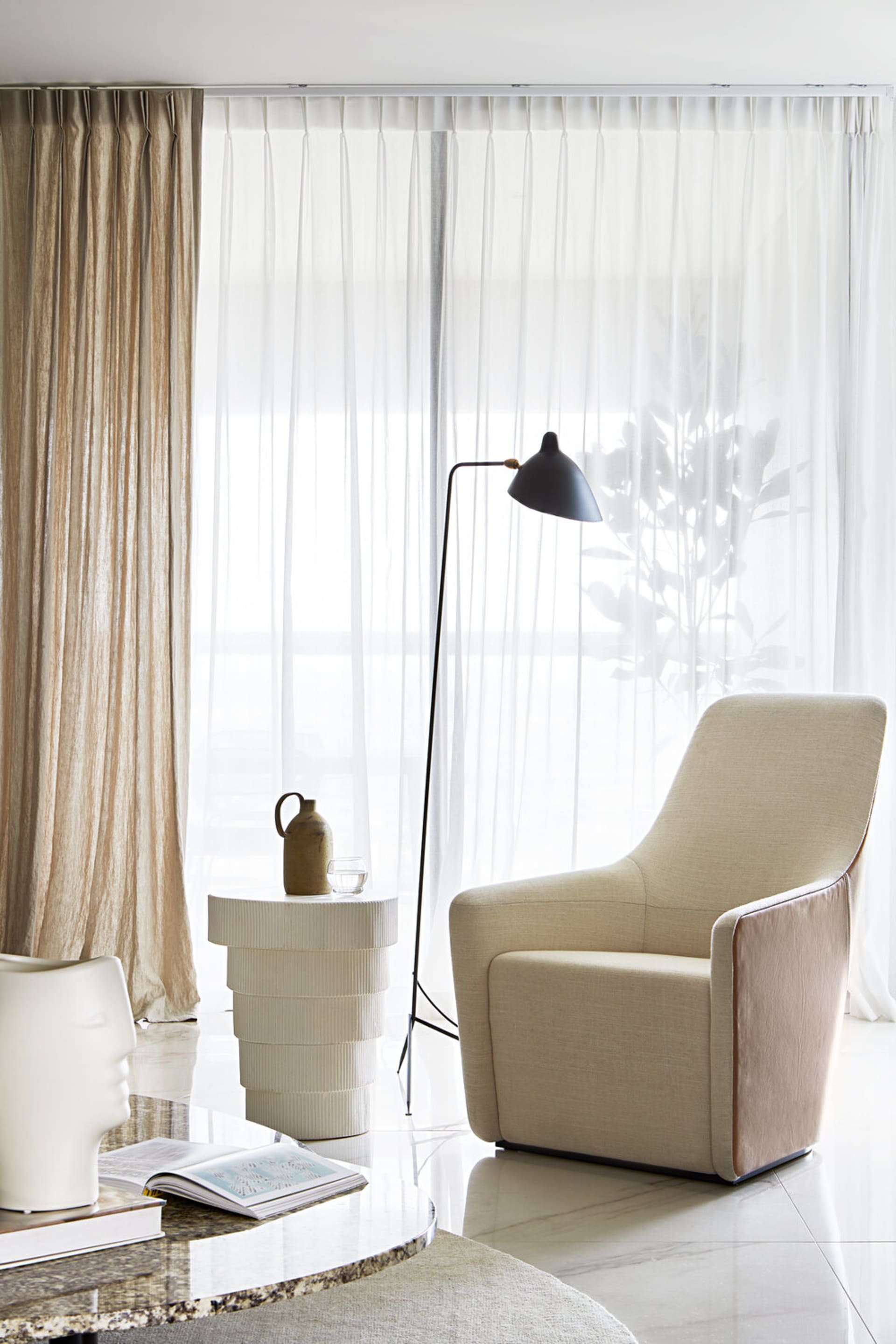 A modern living room with a textured white curtain, lamp, and upholstered chair near a window.