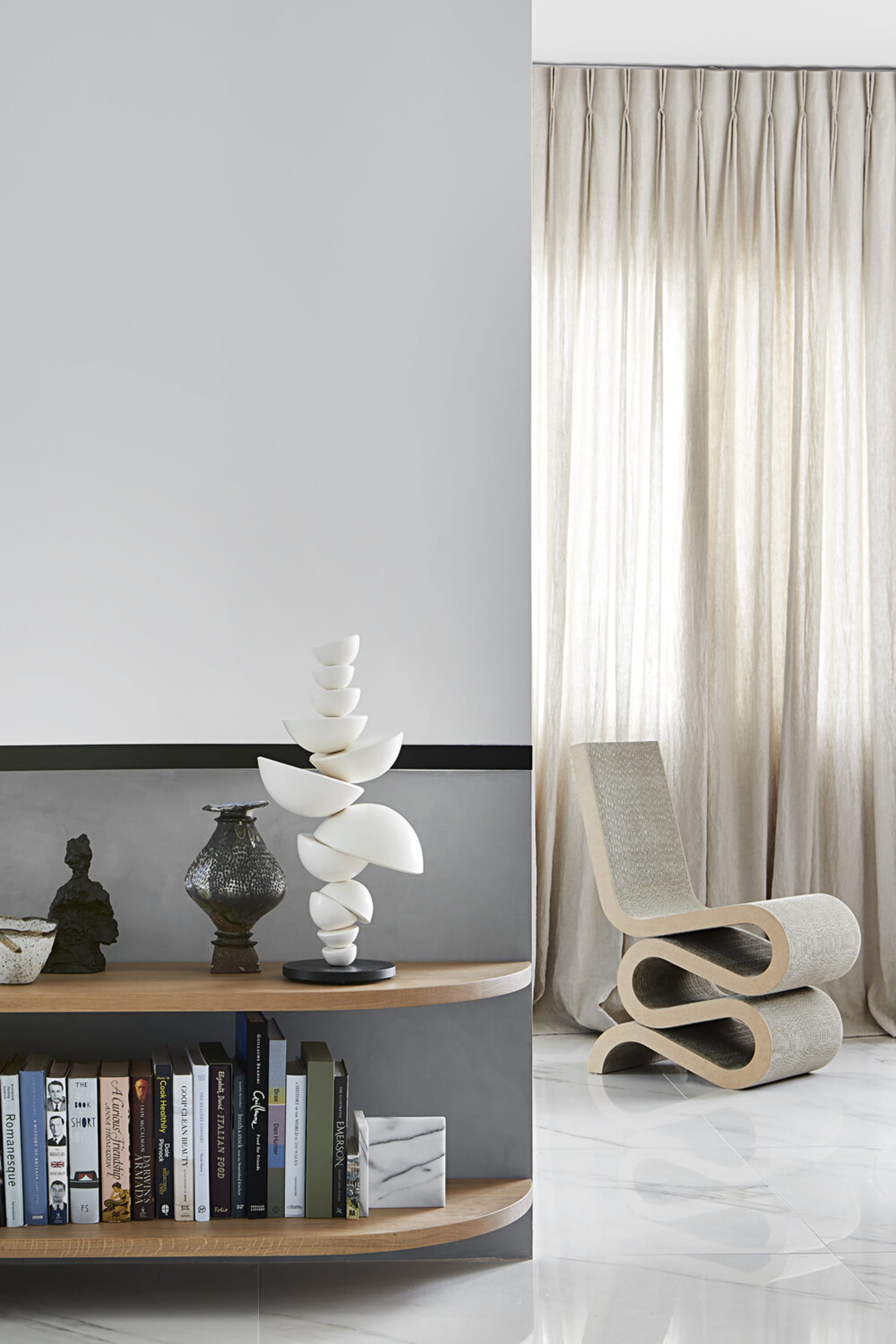 A modern living room features a curved wooden bookshelf with marble accents, a contemporary white sculpture, and a fabric-cov