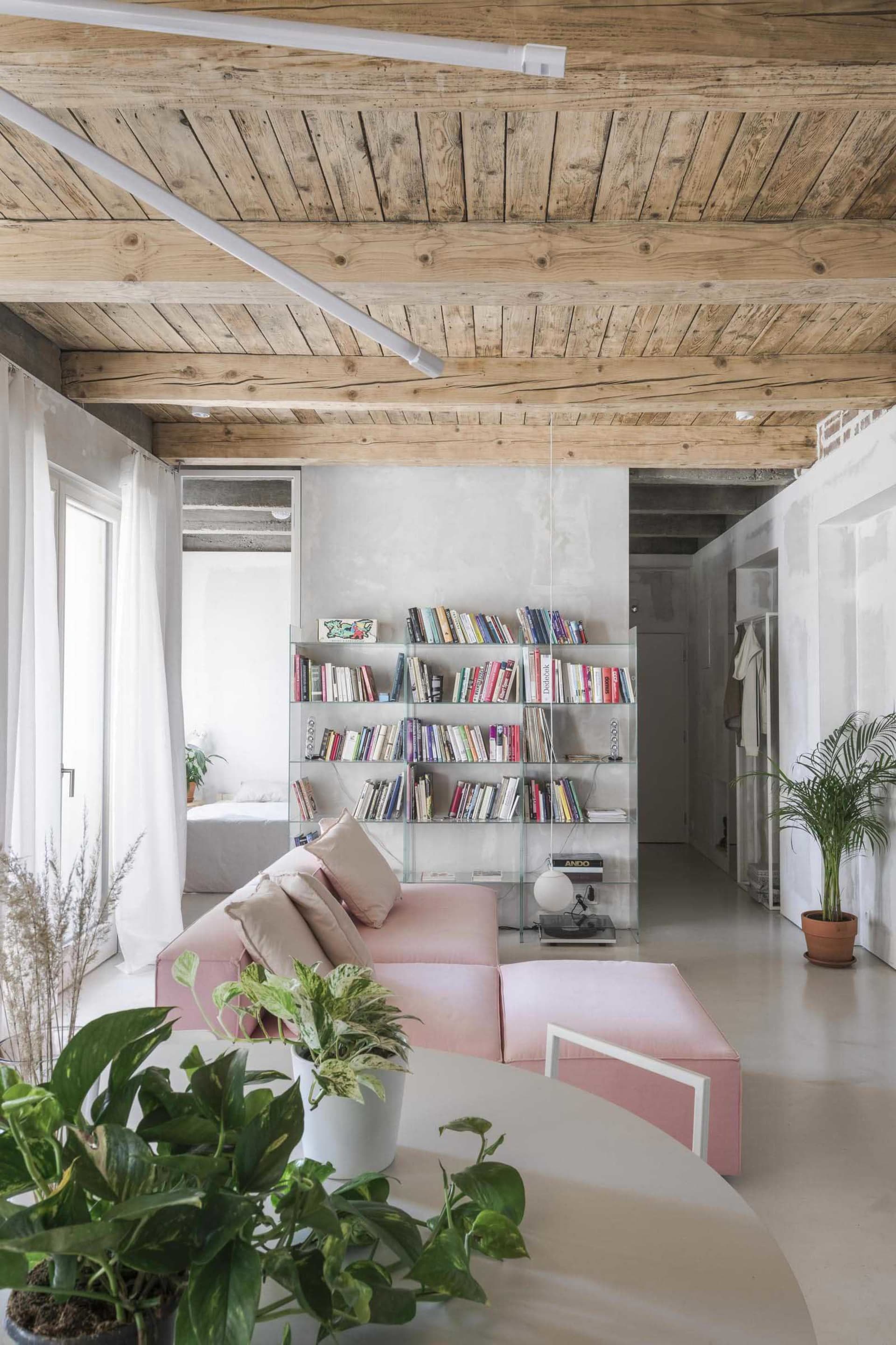 Minimalist living room with glass shelves, concrete flooring, and pink upholstered furniture.