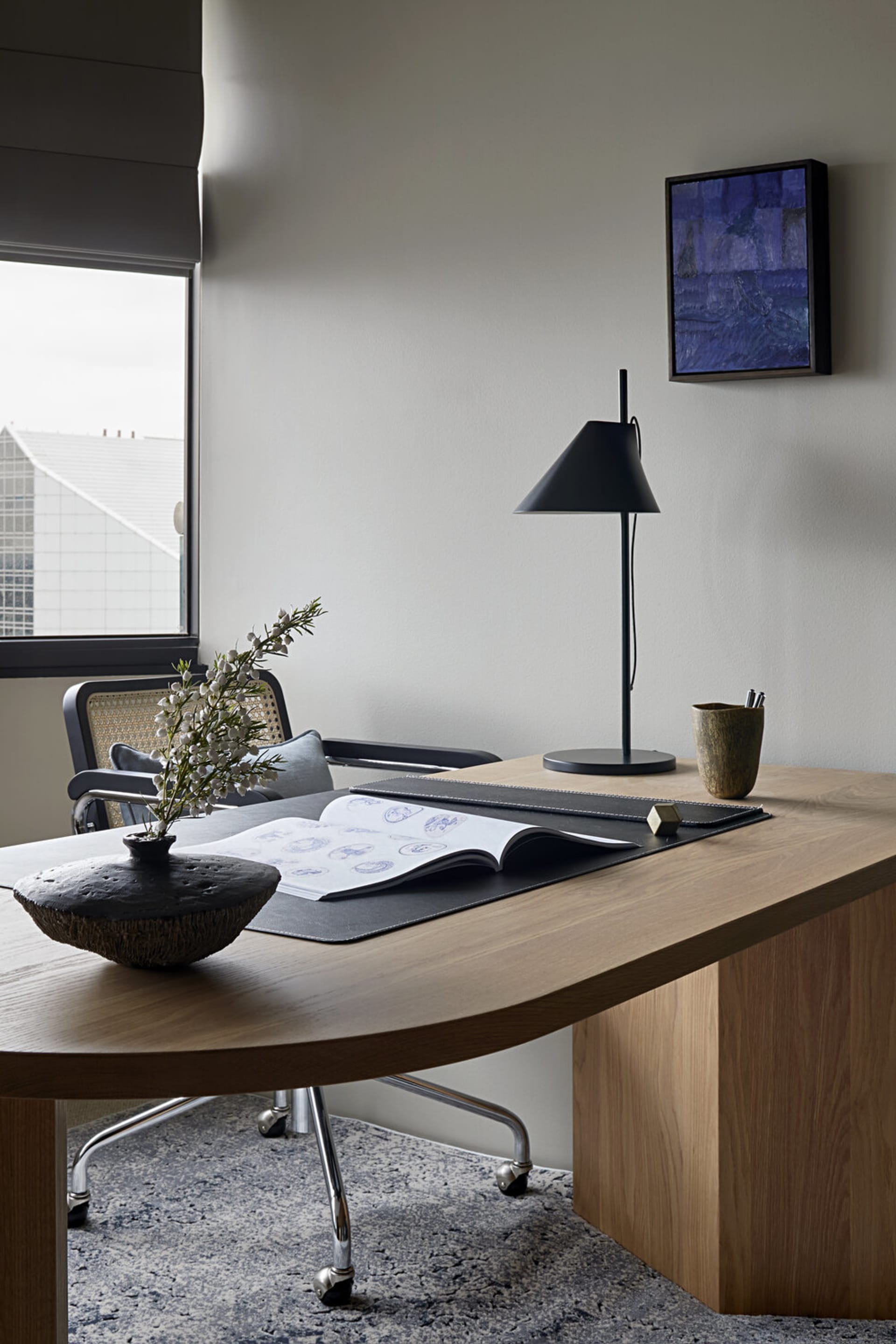A modern office desk space featuring a wooden desk with a lamp, a sketchbook, and a chair.
