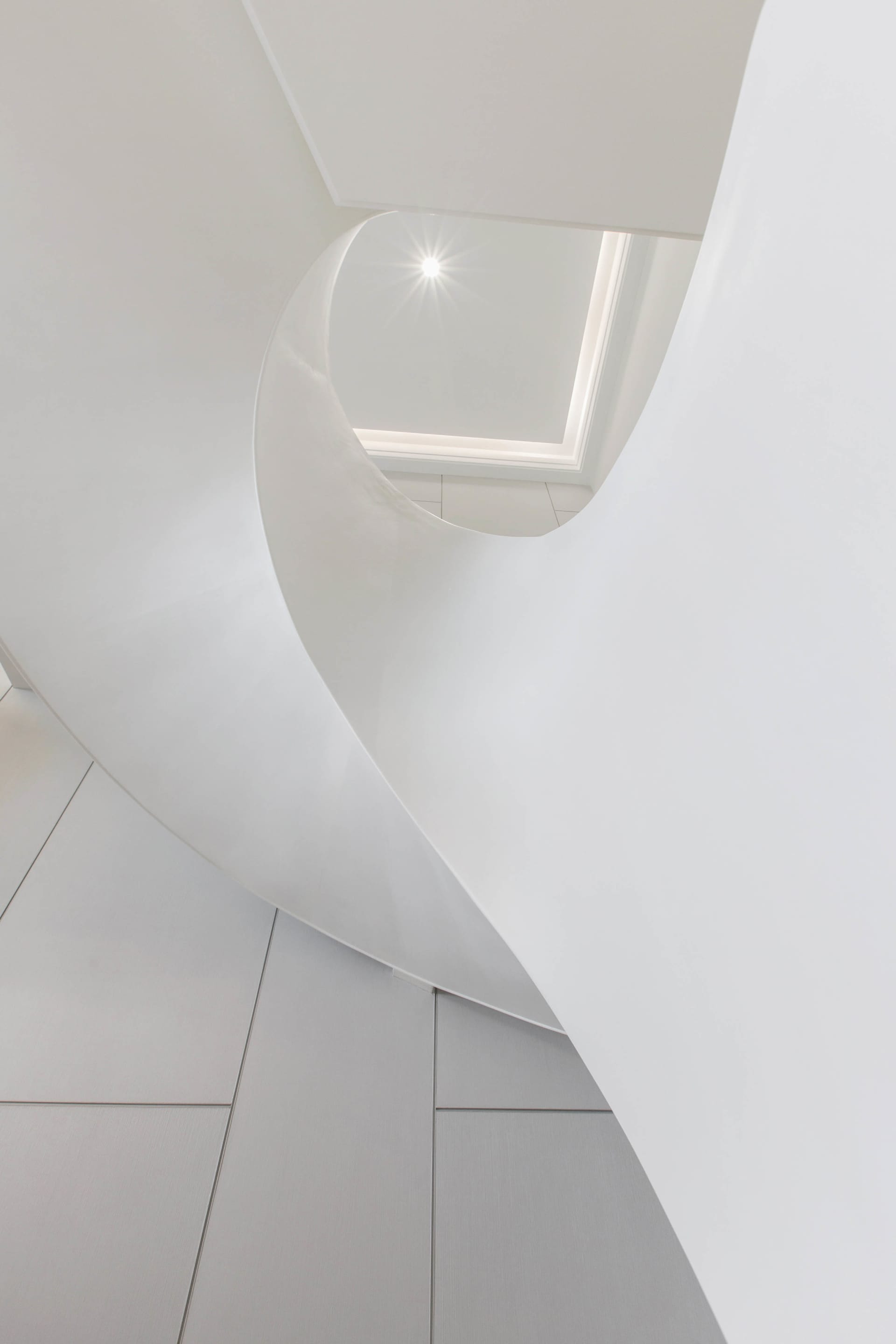 A minimalist white staircase illuminated by natural light from a square skylight.
