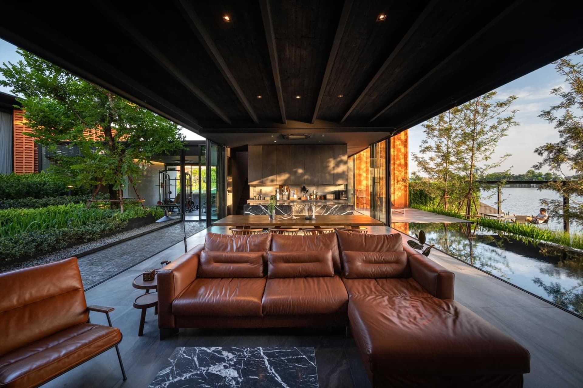 Modern indoor-outdoor luxury living room featuring a leather sofa, marble coffee table, and a pool with a view of the water.