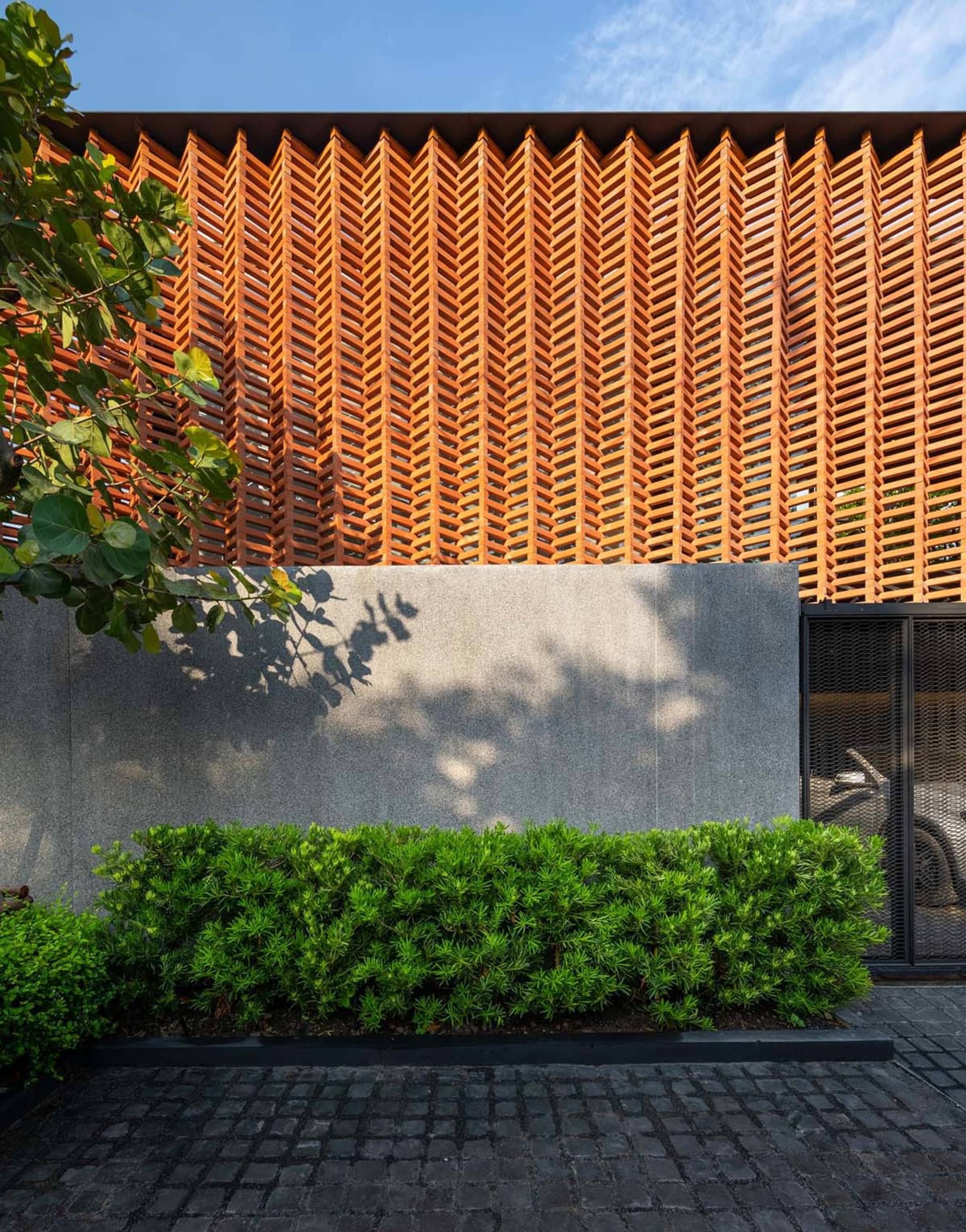 Modern house exterior with wooden lattice, concrete walls, and green hedge.