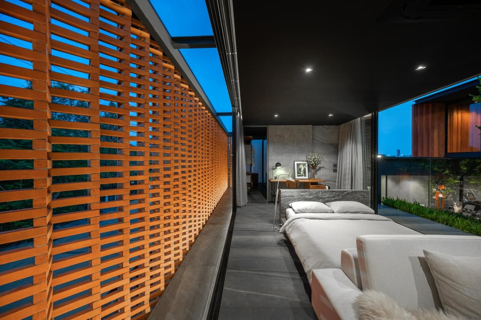 Modern minimalist bedroom with wood and concrete interior, featuring a bed and a reading lamp. Nighttime view.