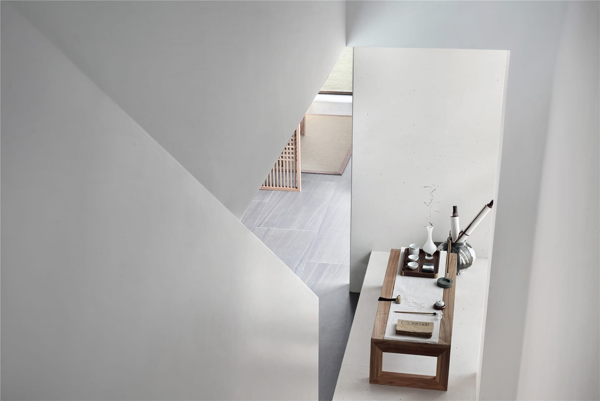 A minimalist bedroom featuring concrete walls and floors with a small table holding a vase and writing implements.