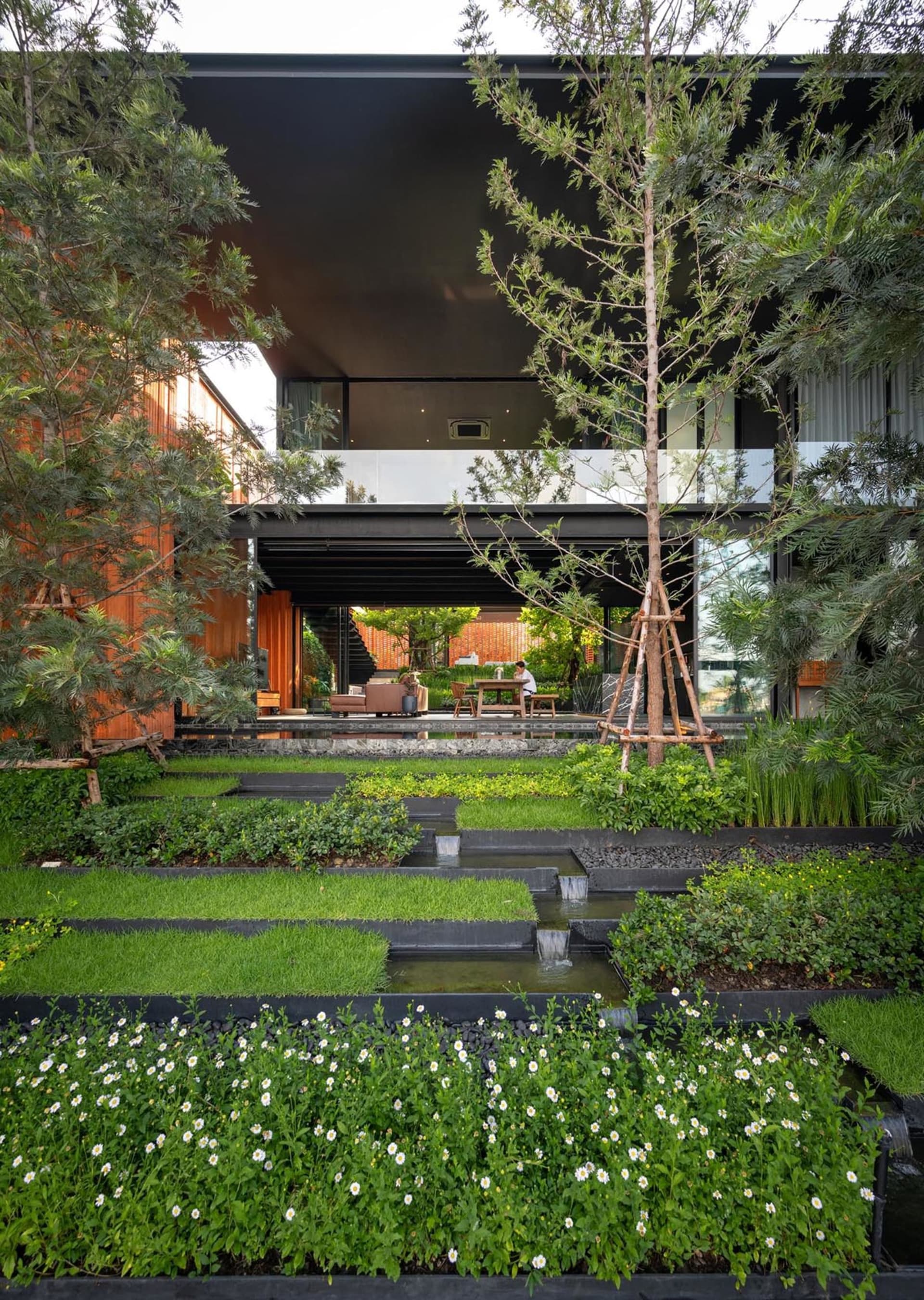 A modern house featuring a concrete exterior with lush landscaping and a water feature.