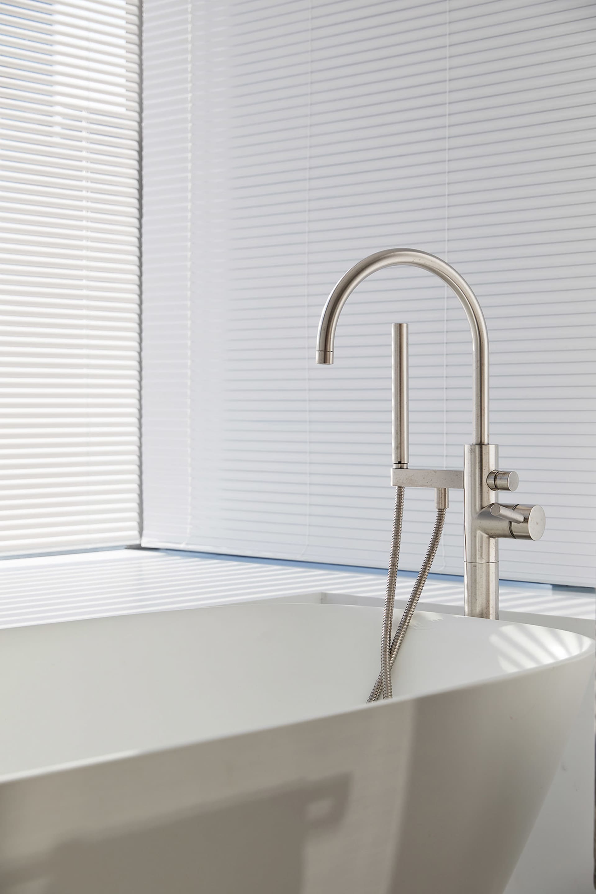 Modern bathroom with a freestanding ceramic bathtub and a sleek, minimalist stainless steel faucet against white vertical bli