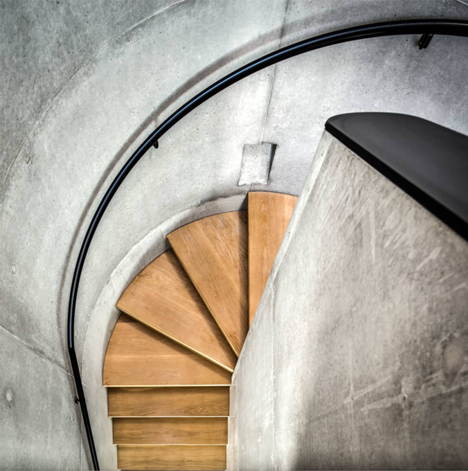 Wooden staircase with a modern design, featuring steel banisters on a concrete wall.