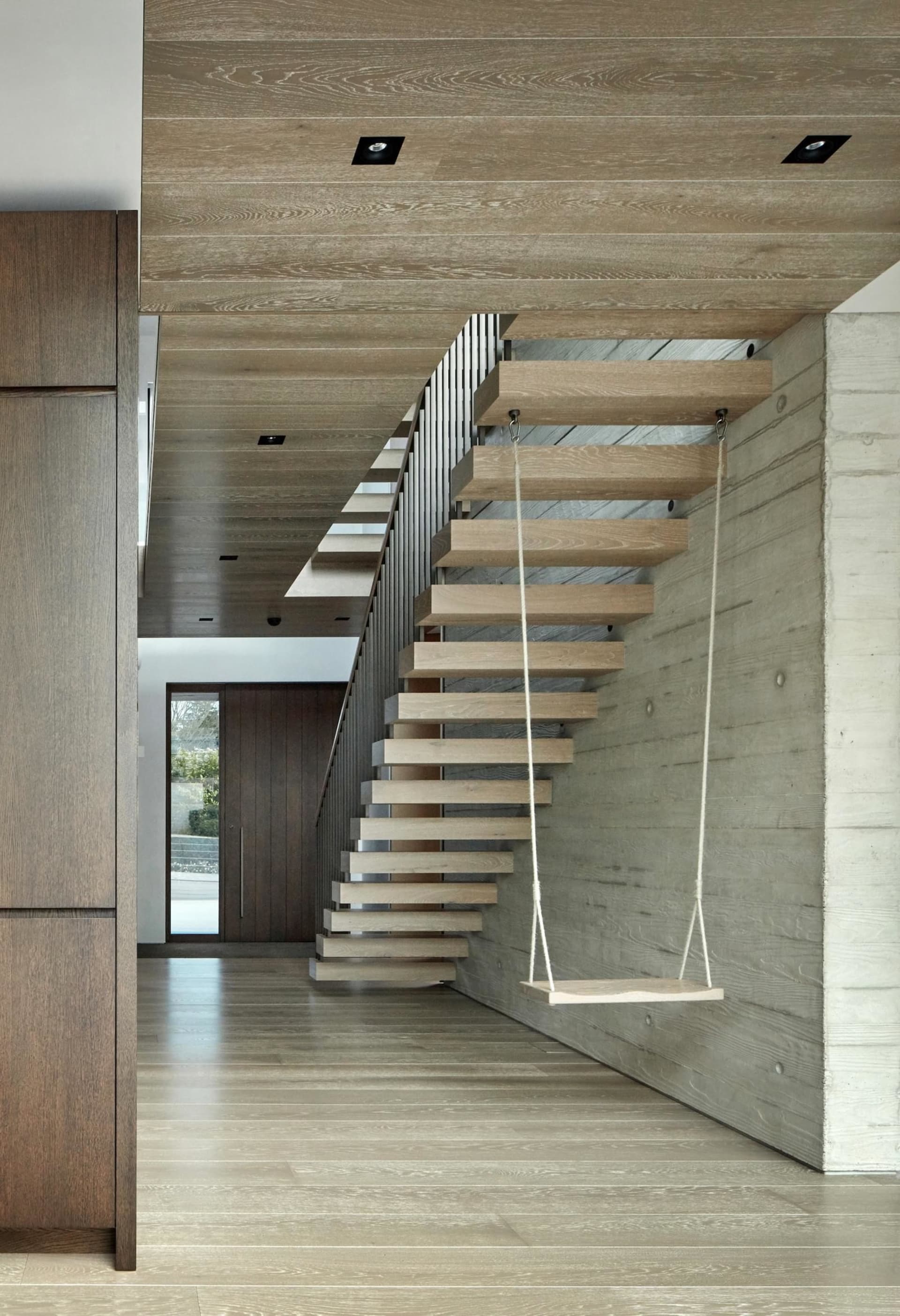 Modern floating stairs with wooden steps and a floating wooden shelf attached to the side wall, illuminated by recessed light