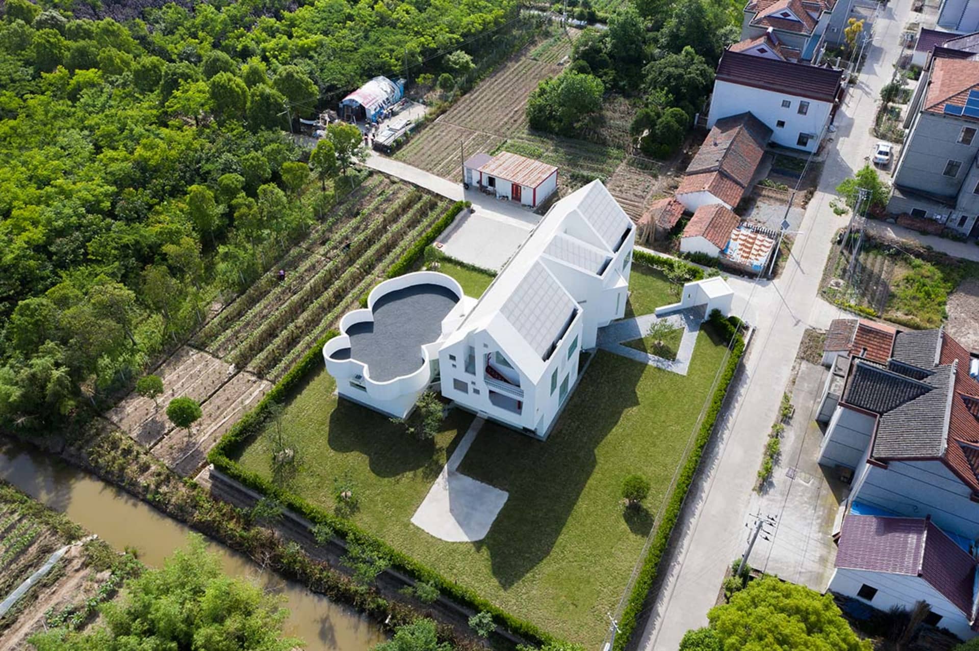 一座擁有白色混凝土外牆的現代住宅,周圍環繞綠意並設有小型泳池。