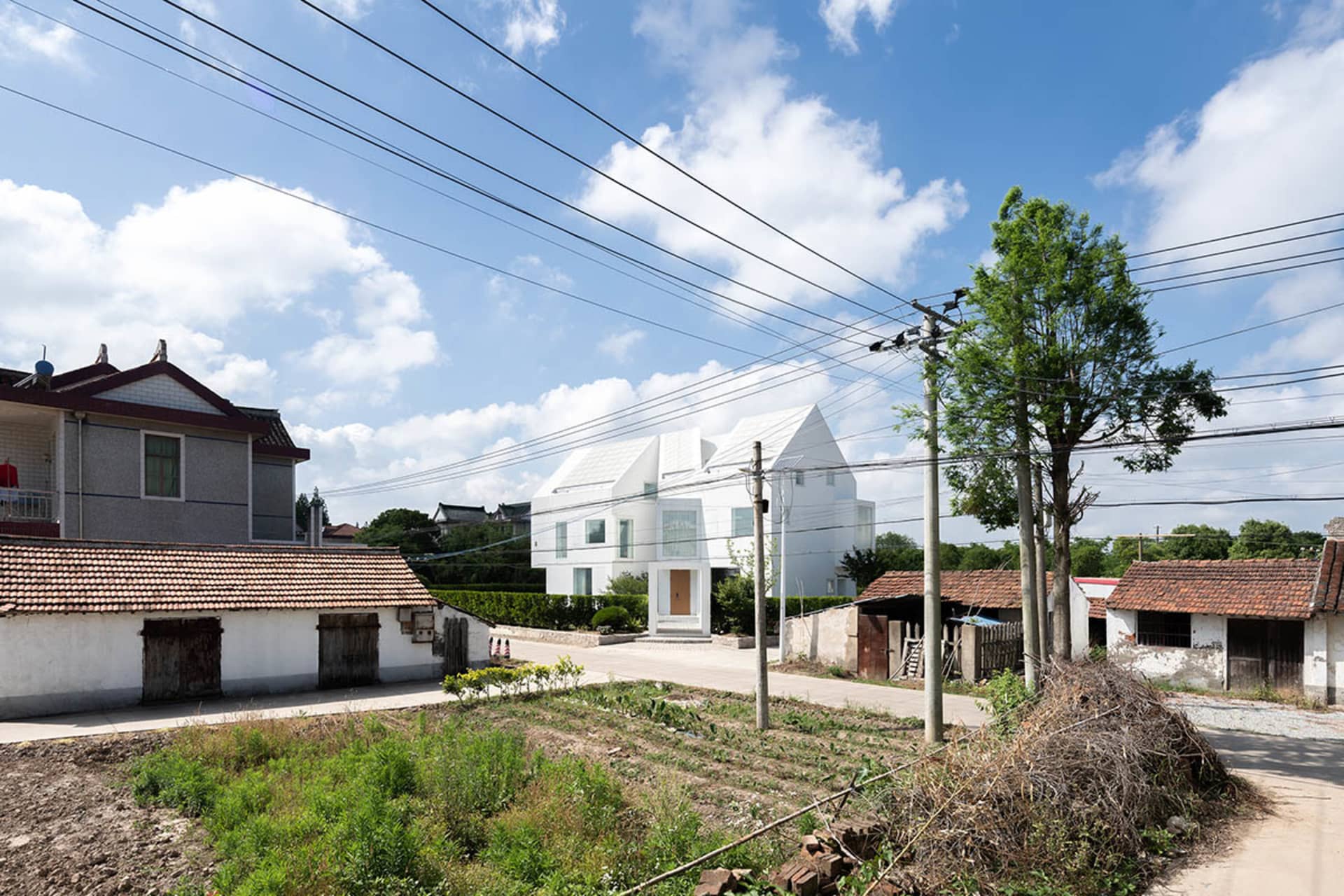 A modern white house with a roof garden, set against a backdrop of greenery and blue sky with clouds.