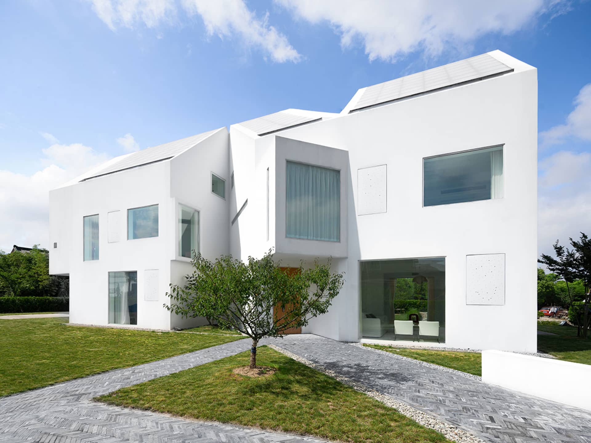 一座現代住宅建築外牆全塗白色，搭配大型玻璃窗與屋頂太陽能板。