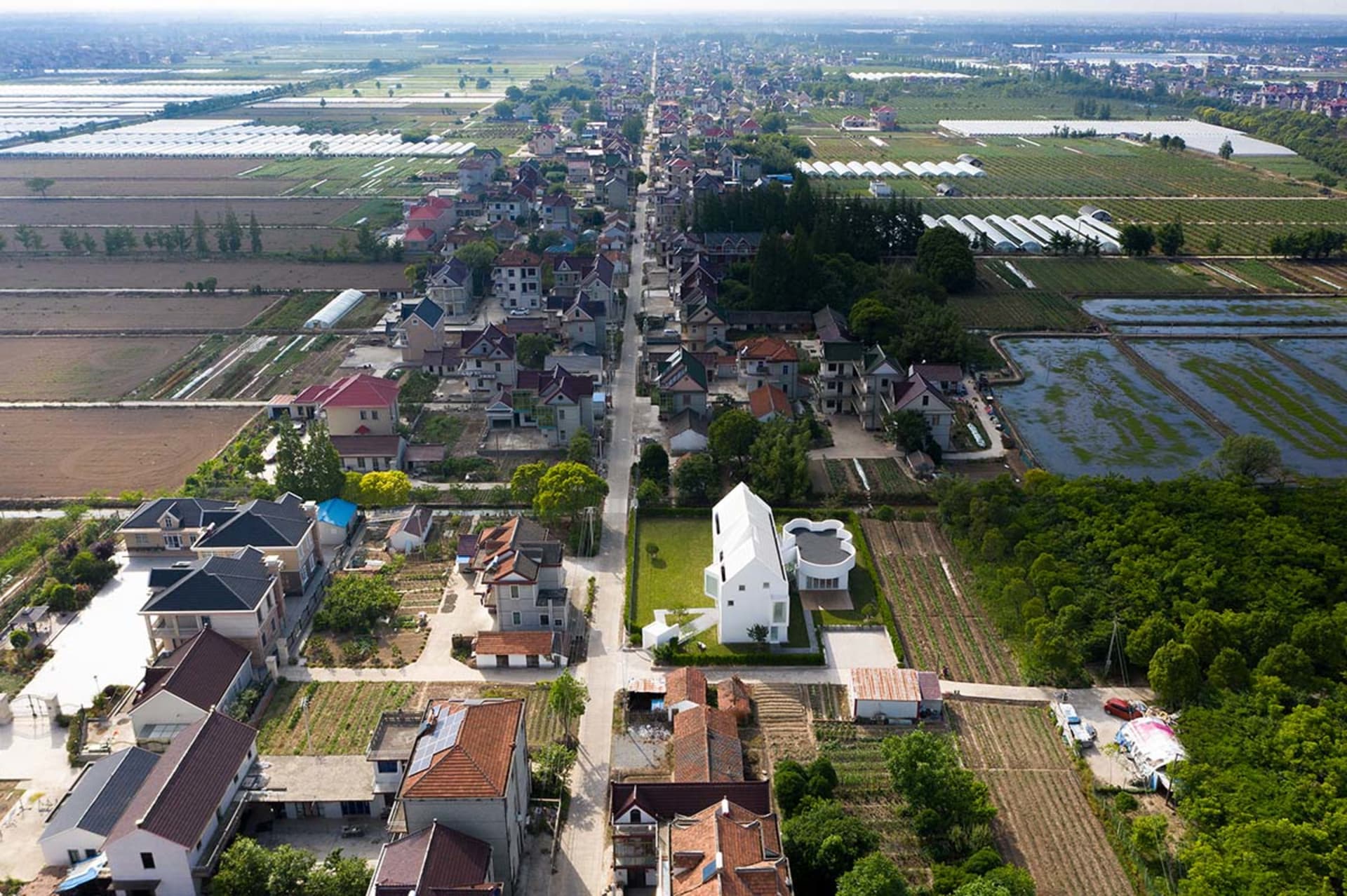 Aerial view of a residential area surrounded by agricultural fields and a road running through the center.