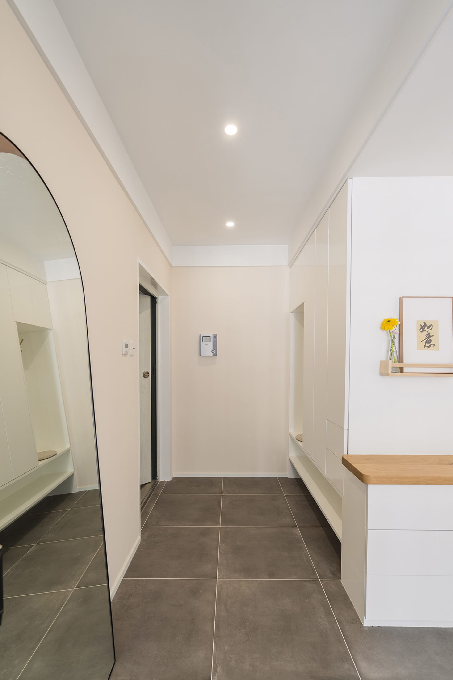A modern entrance hall featuring ceramic tiles on the floor and walls, with white cabinets and a large curved mirror.