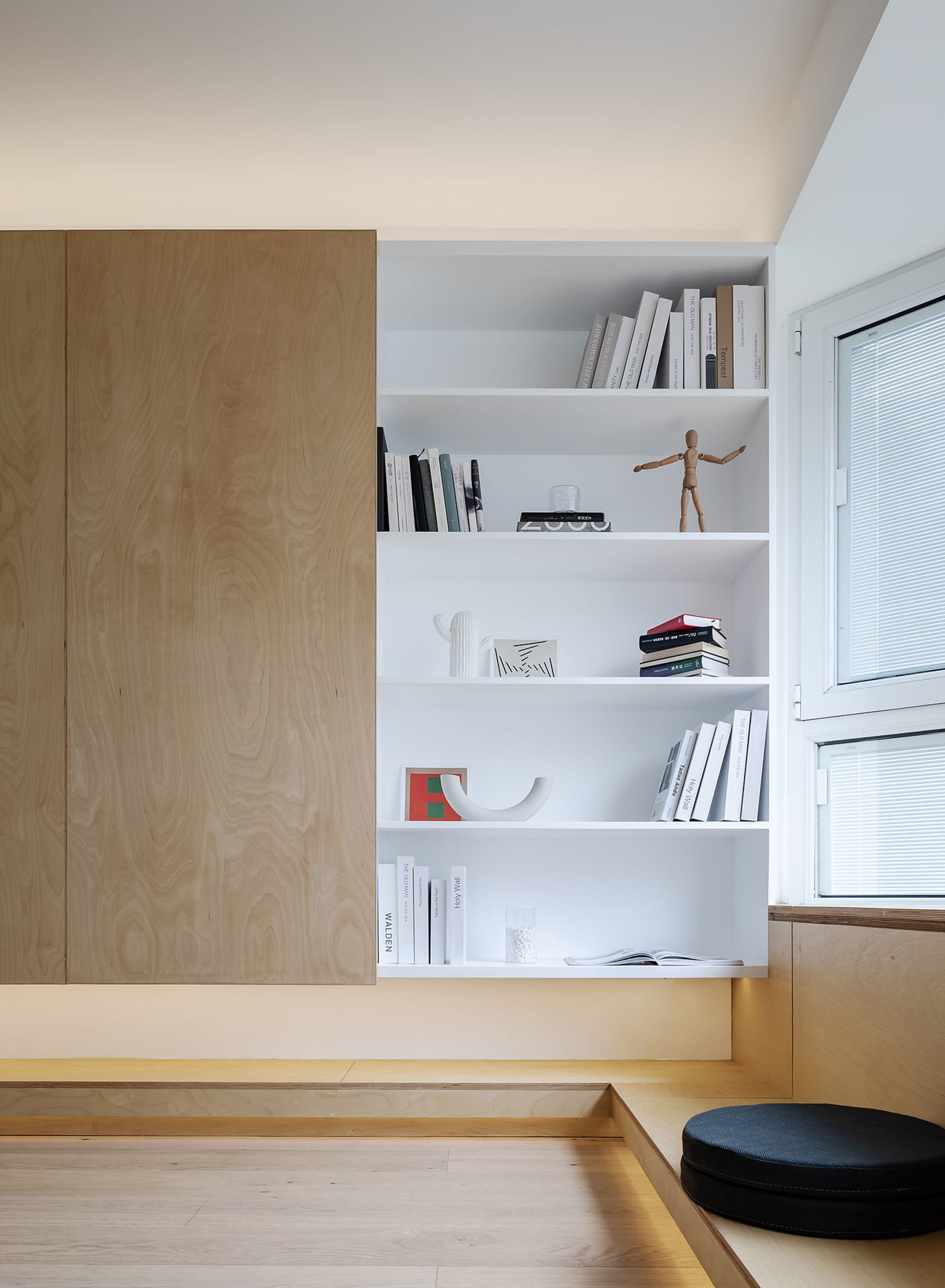 A modern minimalist living room with white shelves featuring books and a wooden figurine, illuminated by soft ambient lightin