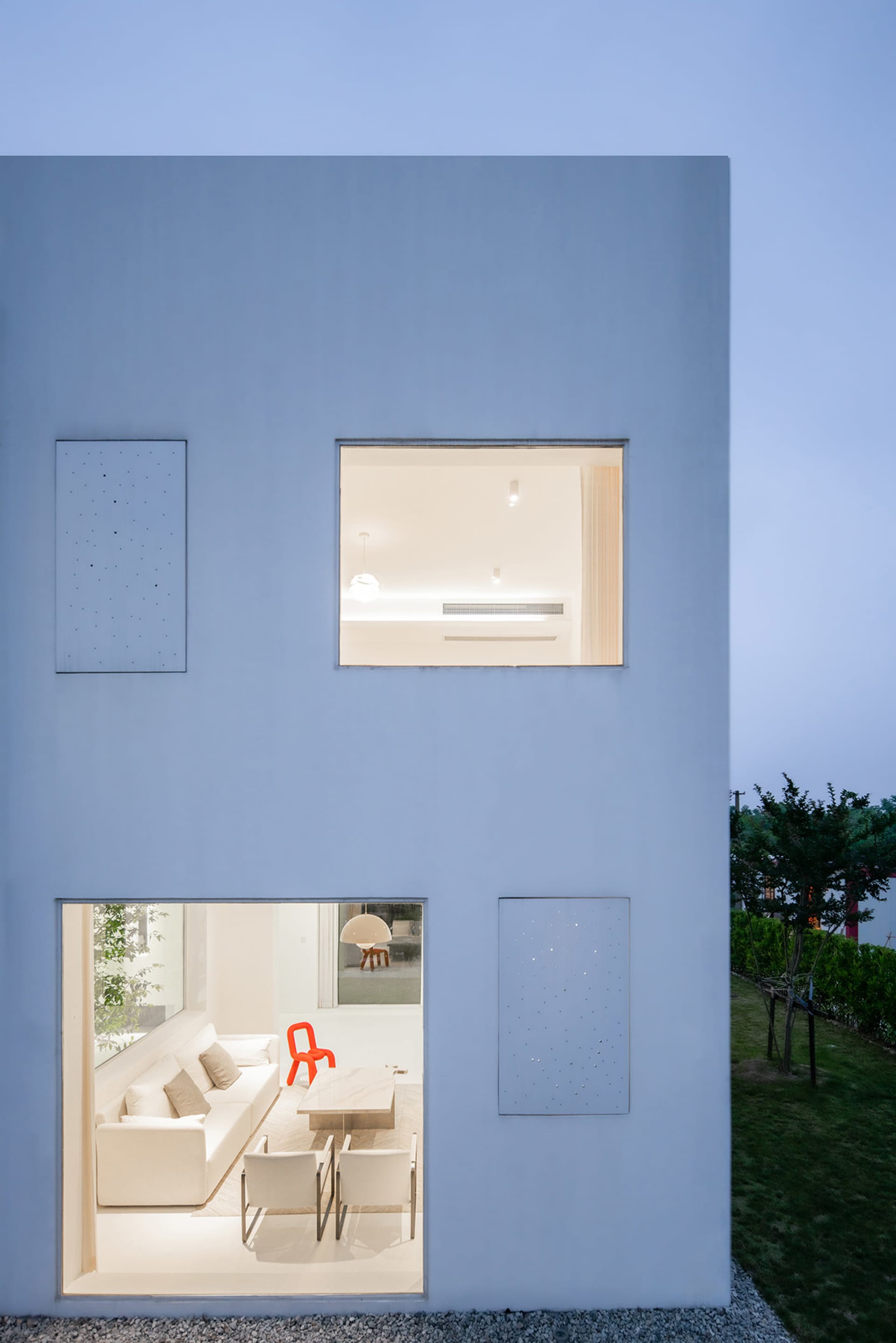 A modern residential exterior featuring a white-painted living room viewed through a window.