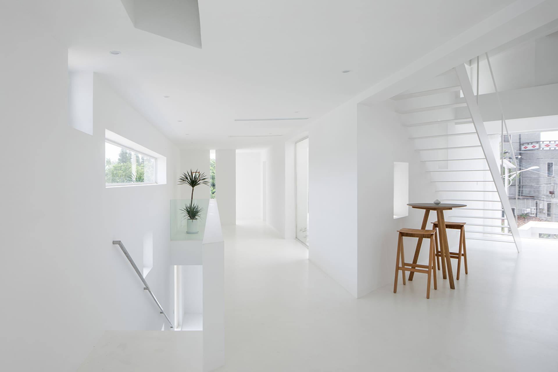 A modern white interior featuring a glass wall, metal railing, and wooden stools.