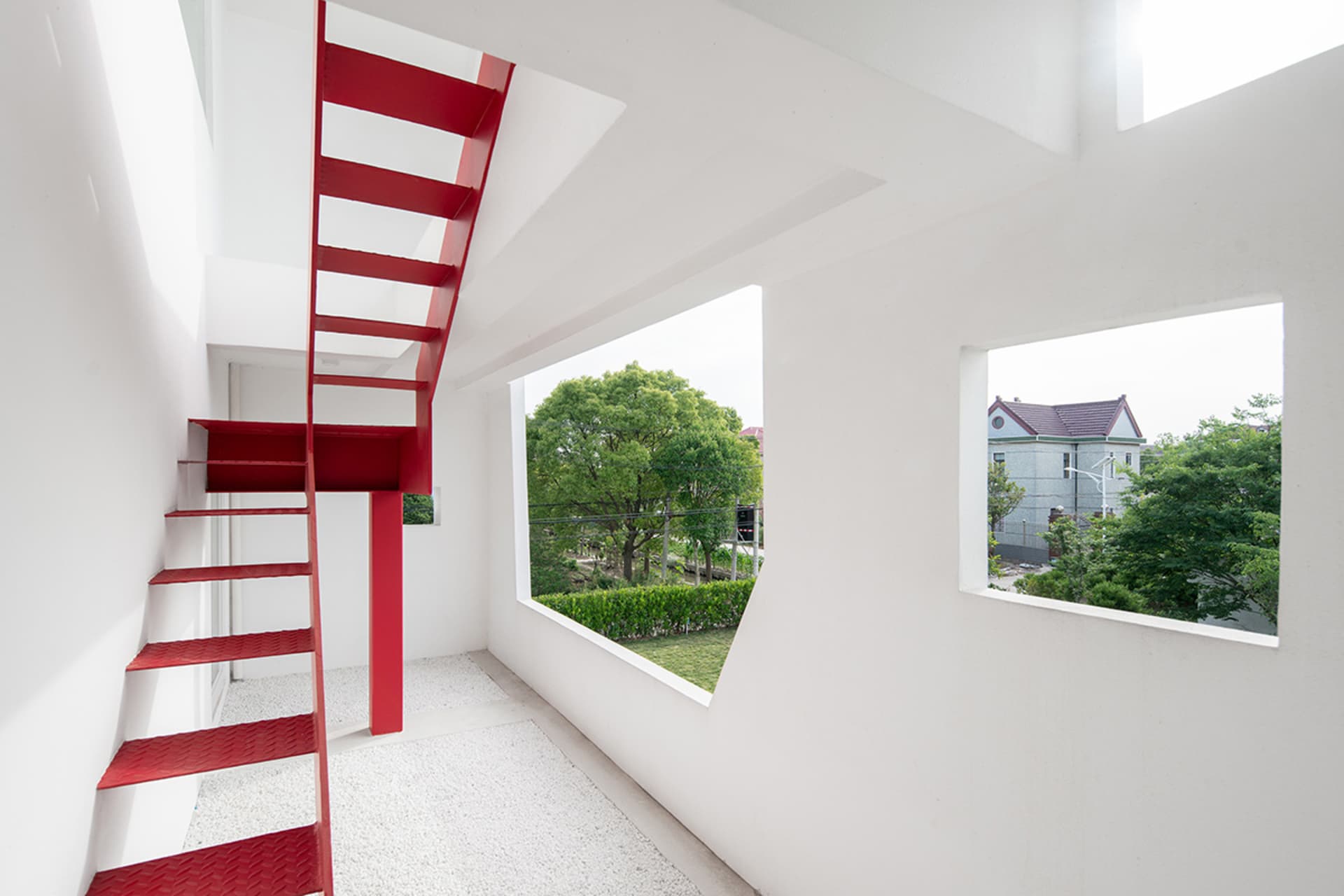 A minimalist, white interior with a striking red metal staircase and large windows.