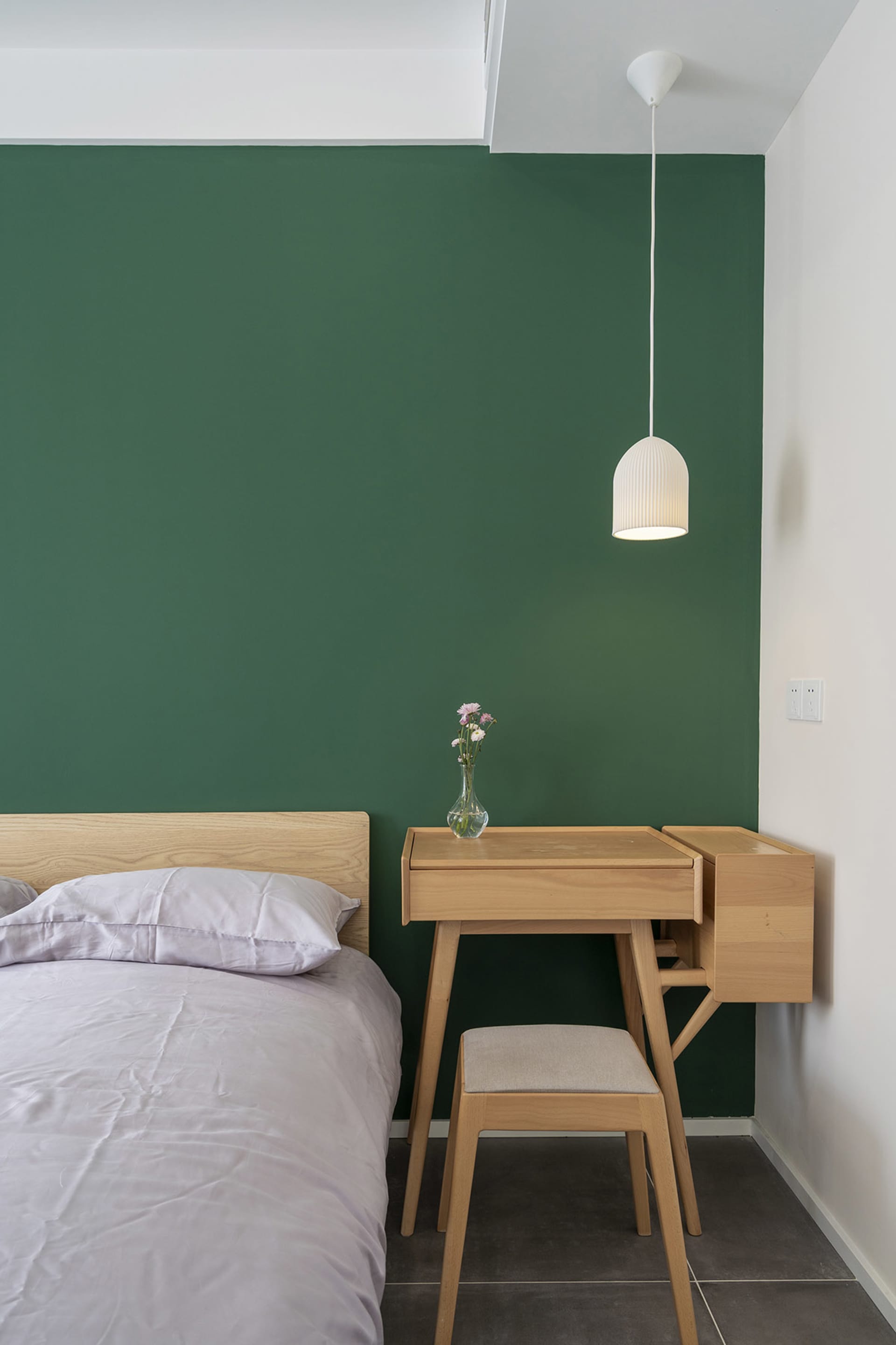 Modern minimalist bedroom featuring wooden furniture, green accent wall, and pendant light above the desk.