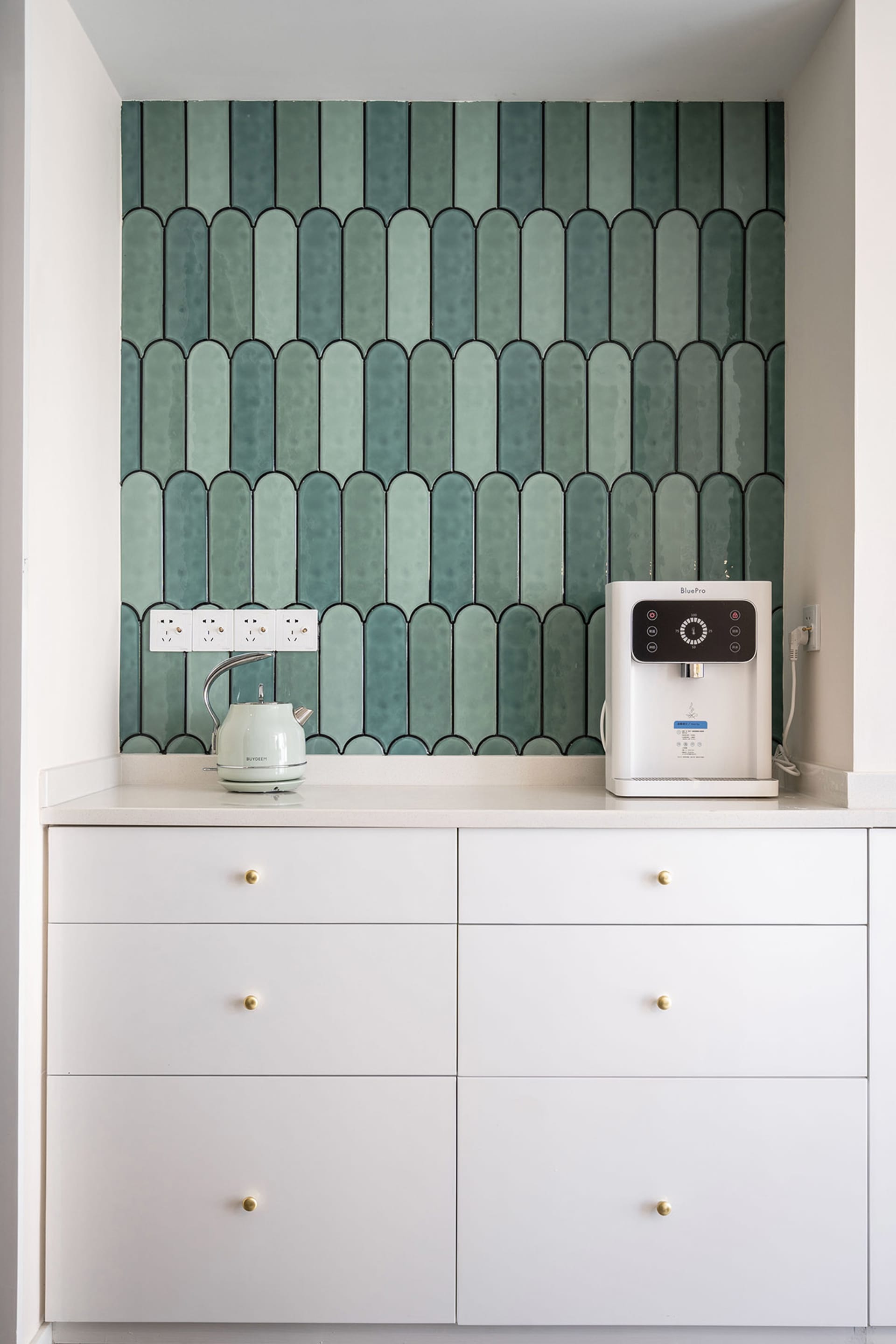 A modern kitchen with white cabinets, green ceramic tiles, and a white countertop.