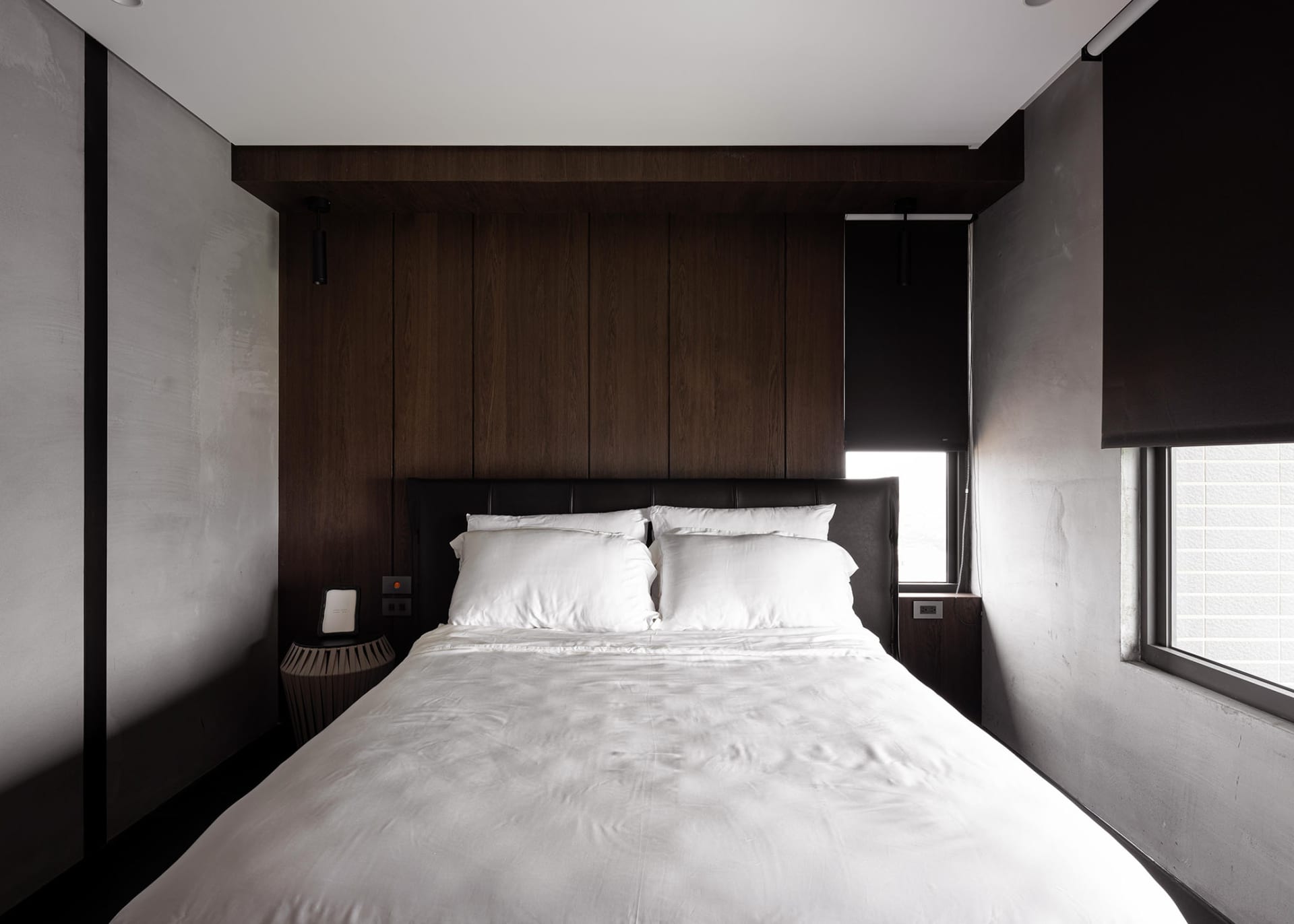 A modern minimalist bedroom with dark wood paneling and white bedding.