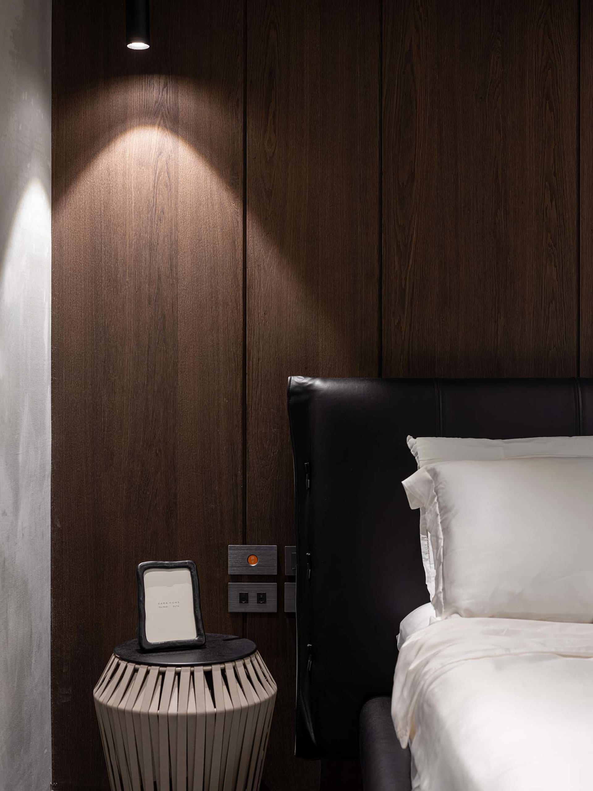 A minimalist bedroom with a wood-paneled wall and white bedding.
