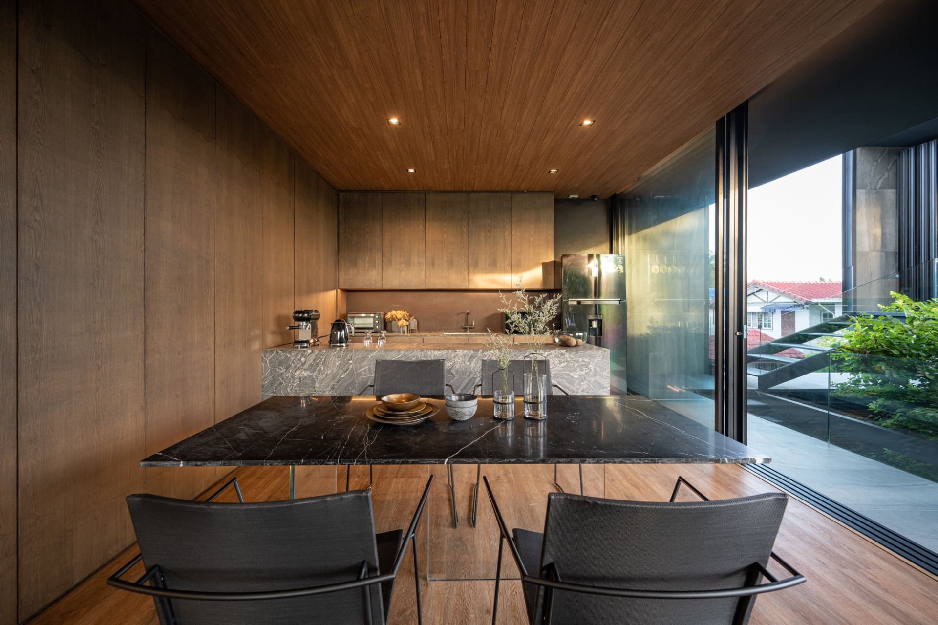 A modern residential kitchen featuring a marble countertop with stainless steel appliances and black chairs.