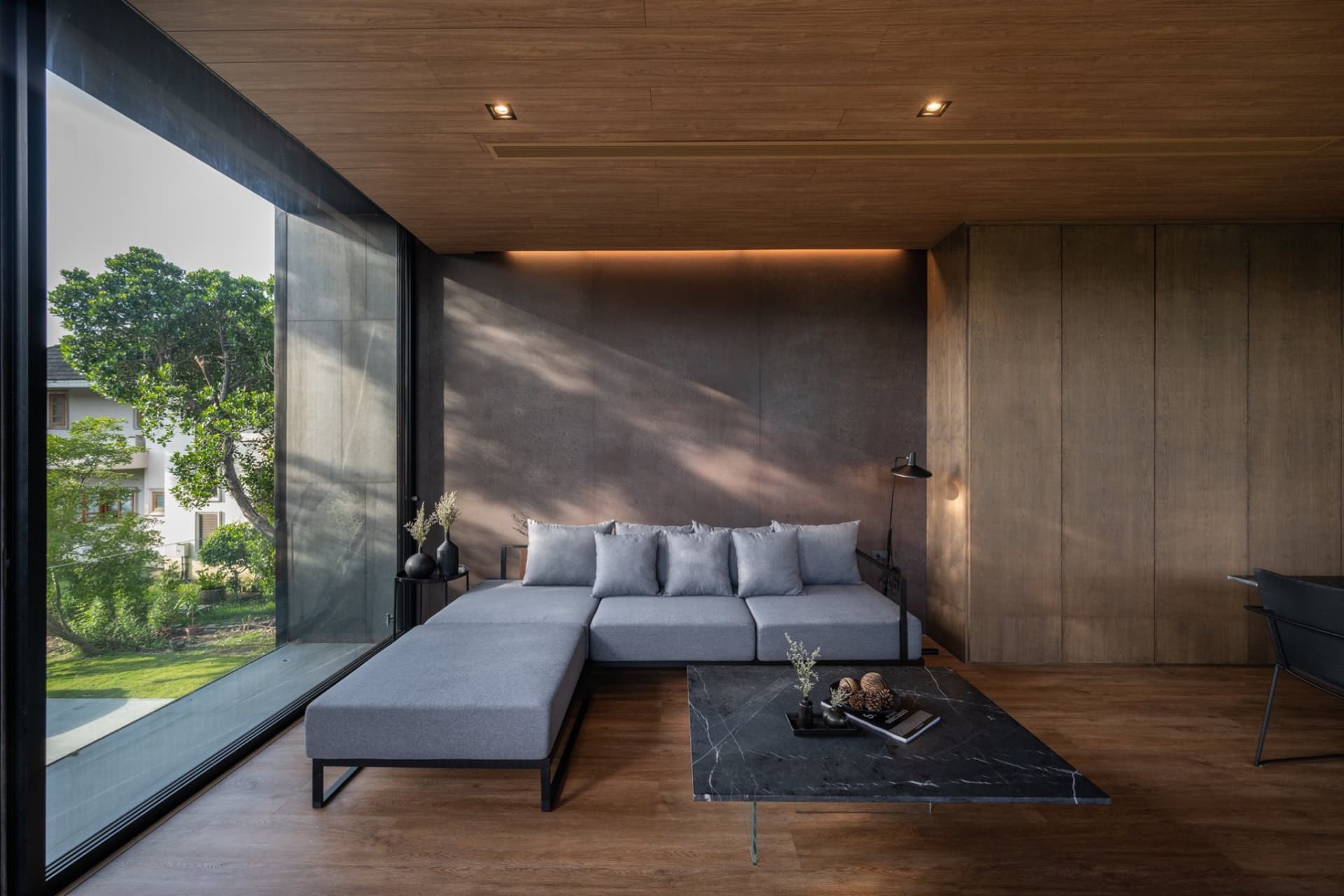 Modern living room featuring a grey sectional sofa with cushions, a black marble coffee table, and a large window overlooking