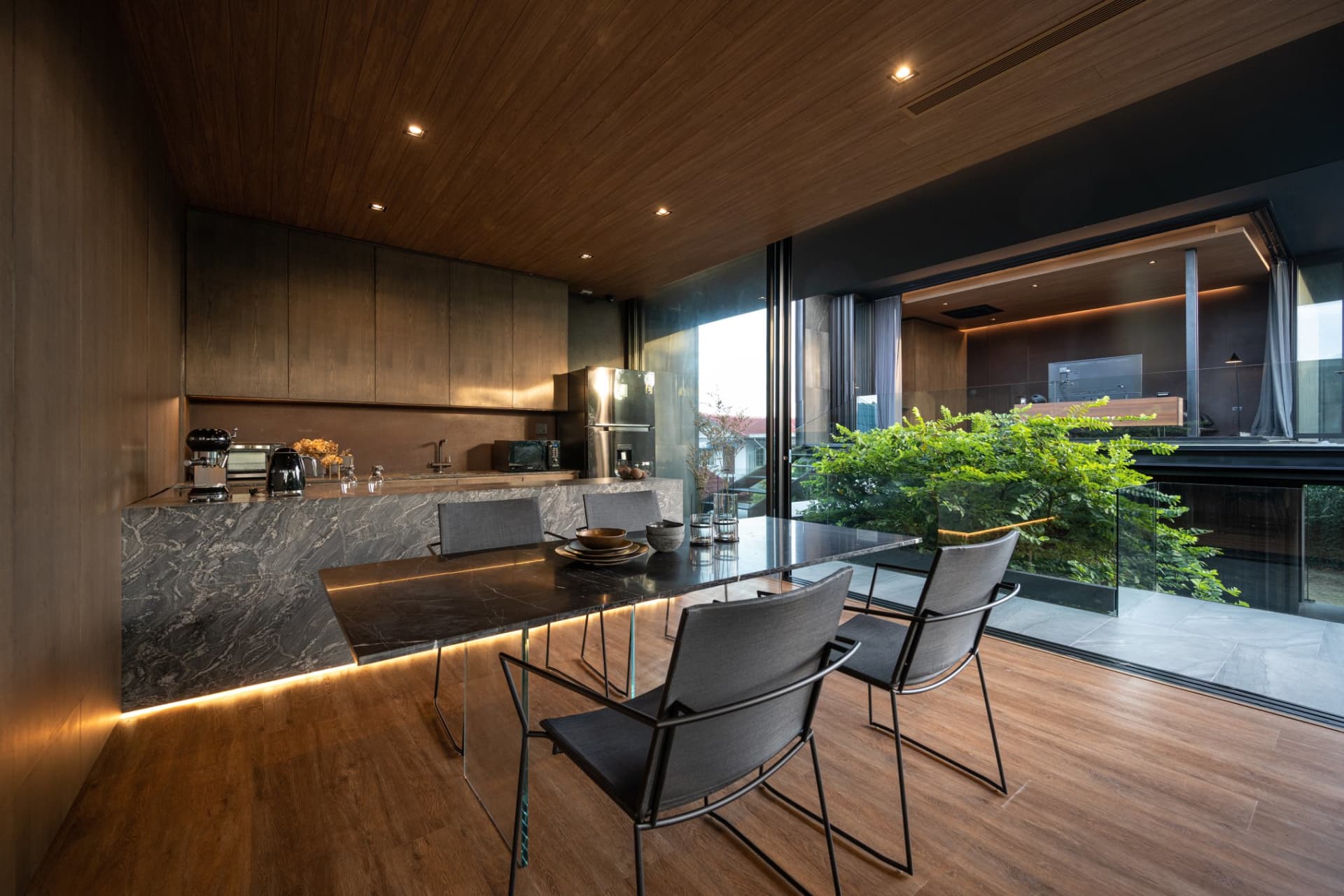 Modern residential dining room featuring a marble table, stainless-steel appliances, and wood finishes.