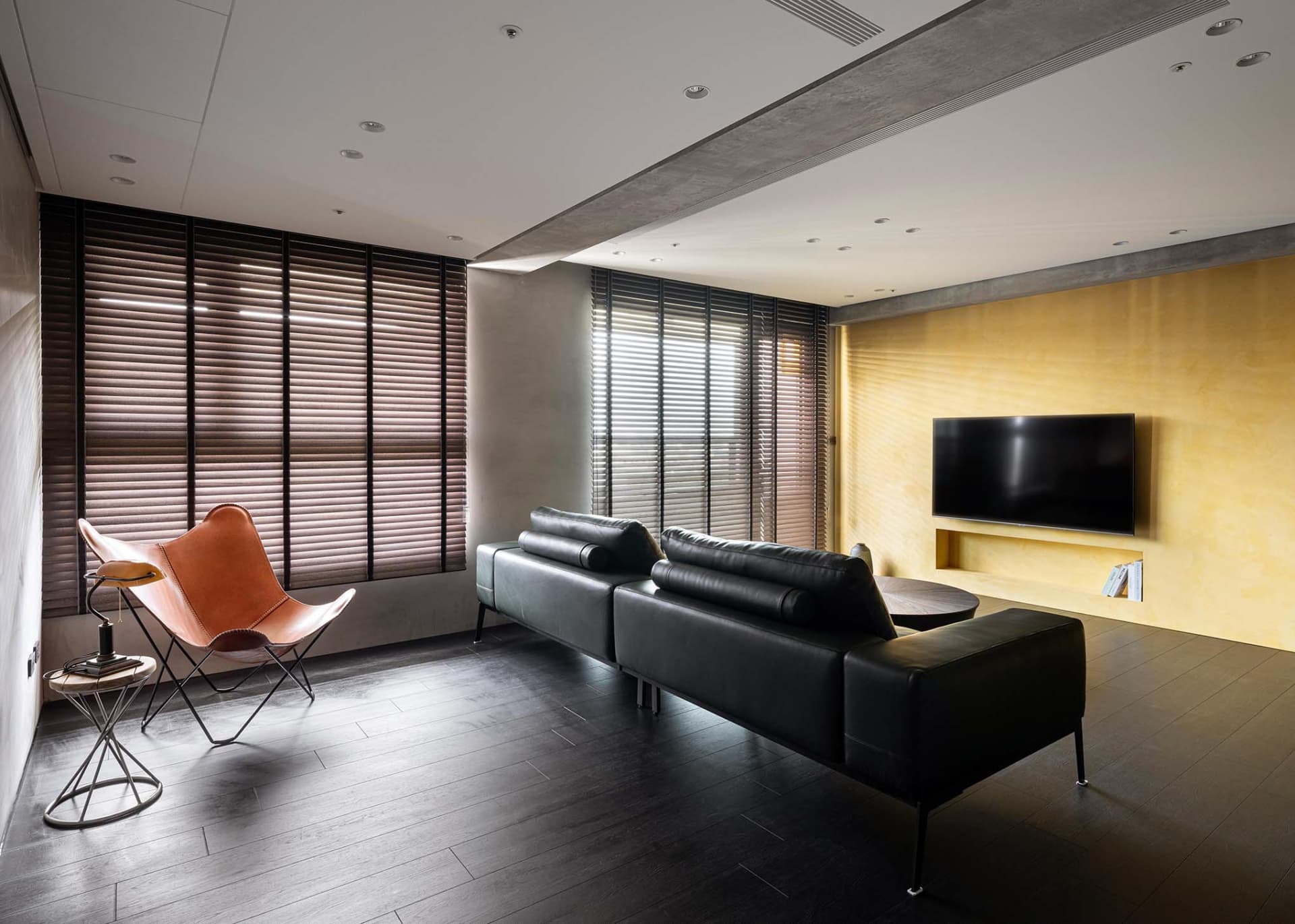 A modern contemporary leather sofa with dark wood flooring and built-in entertainment center, featuring industrial-style meta