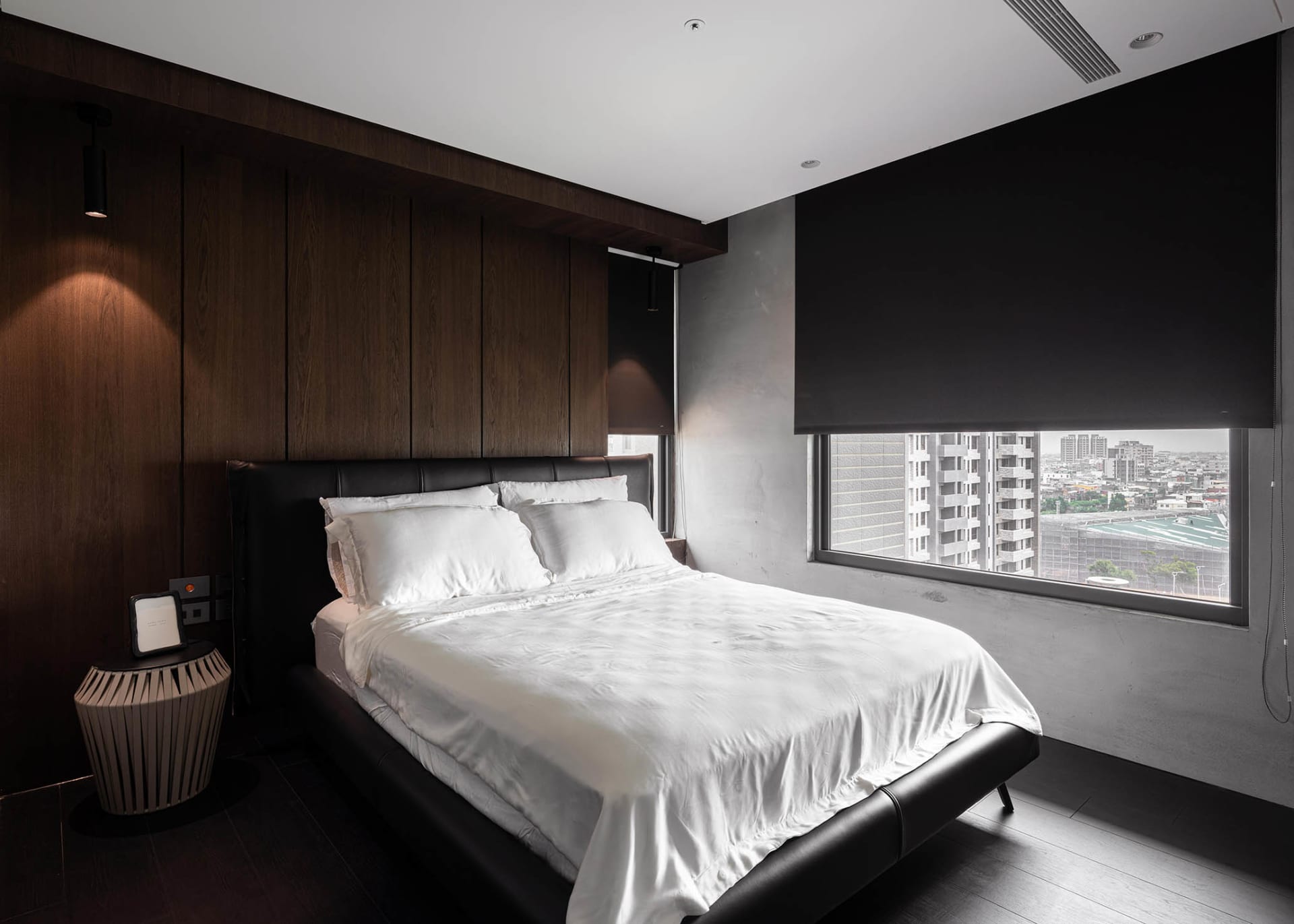 A modern minimalist bedroom with a black leather bed and white bedding, featuring dark wood walls and a large window with a c