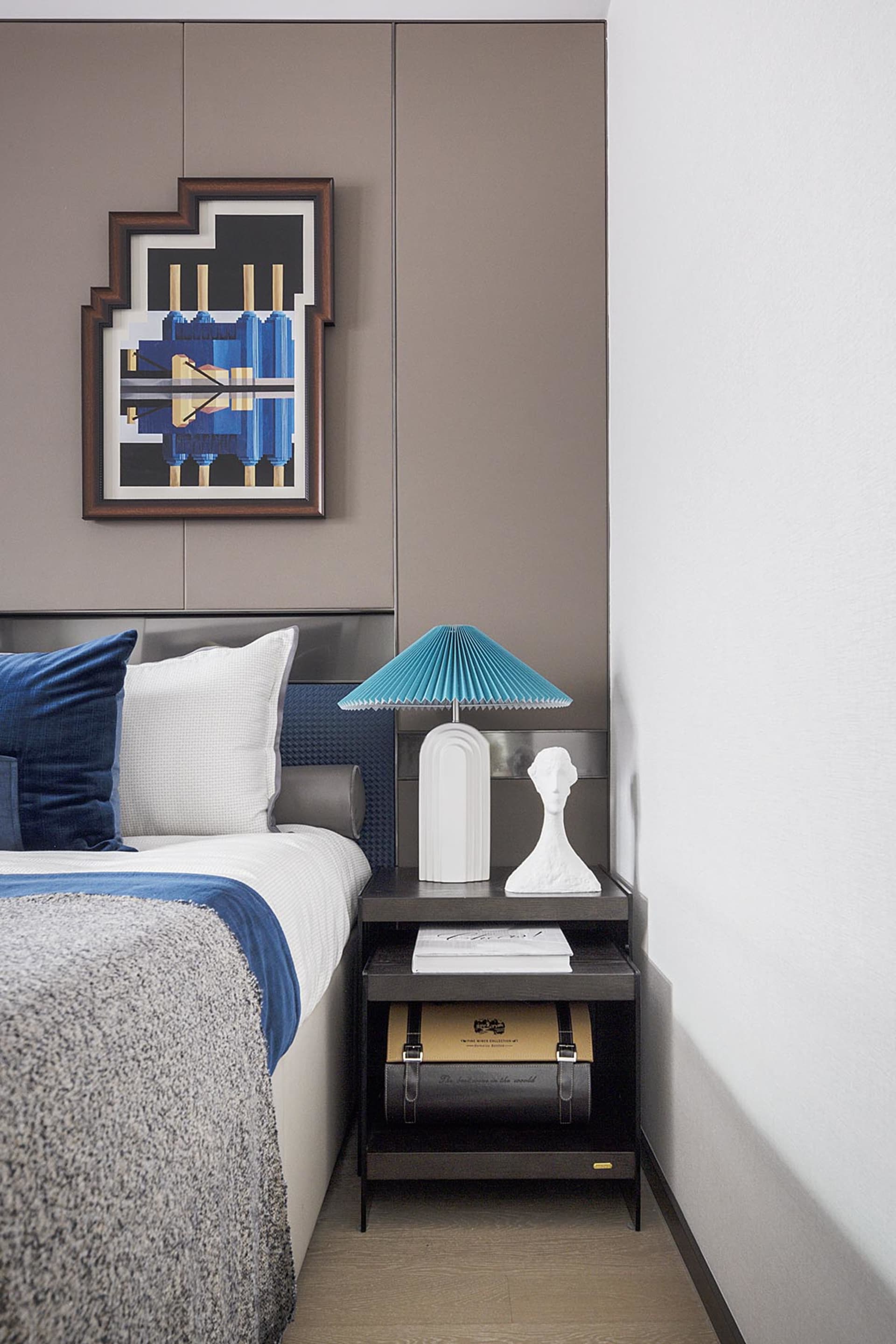A modern bedroom featuring a double bed with blue bedding and white accents, accompanied by a black nightstand with a white l
