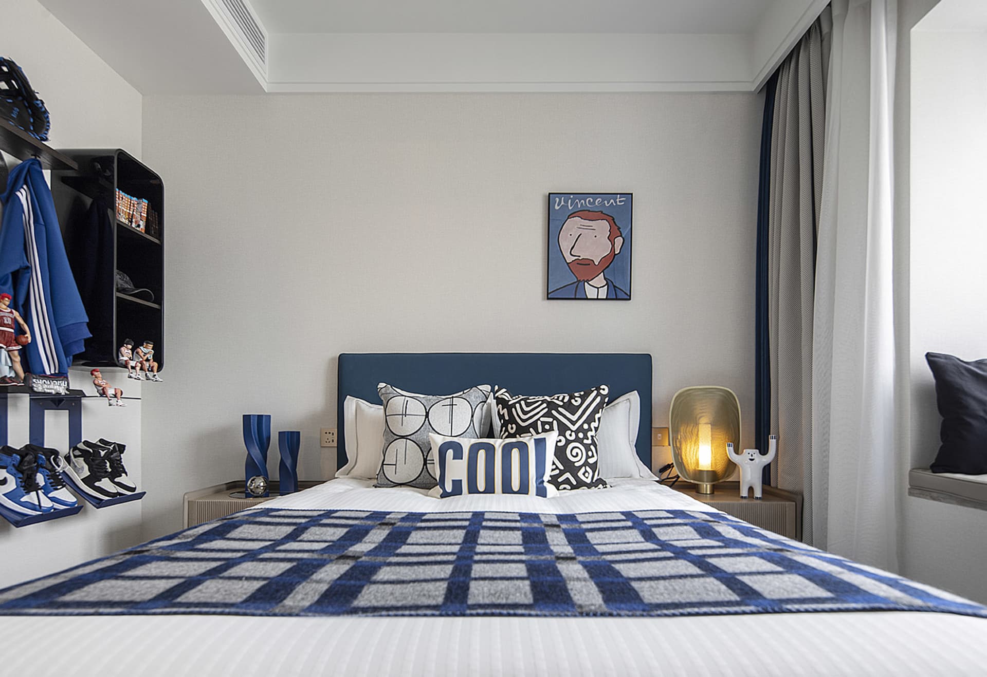 Modern bedroom featuring a white bed with blue and white checkered blanket and decorative pillows placed against a light gray