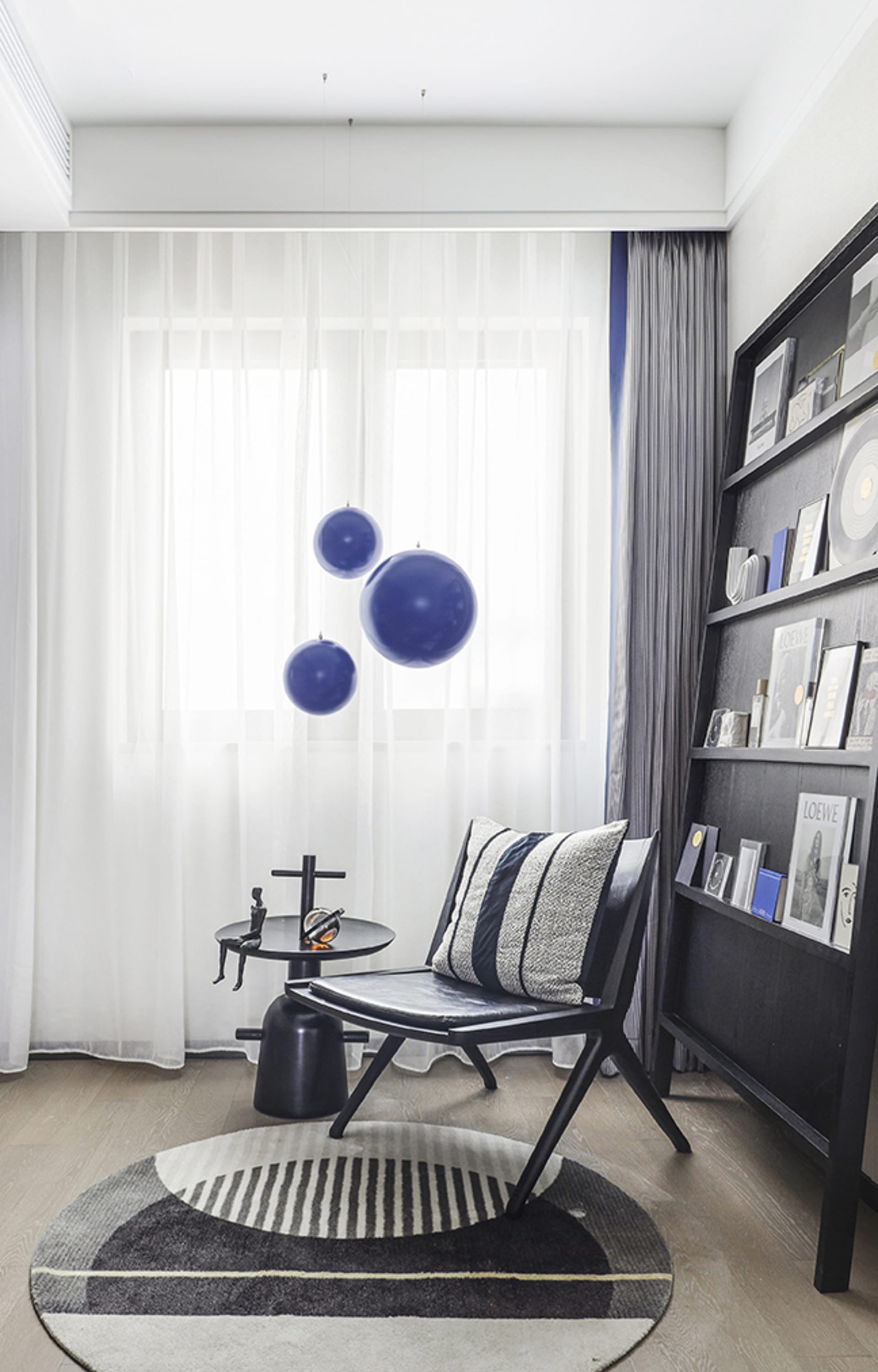 Minimalist living room featuring a black wooden chair, floating blue ball decorations, and a striped rug.