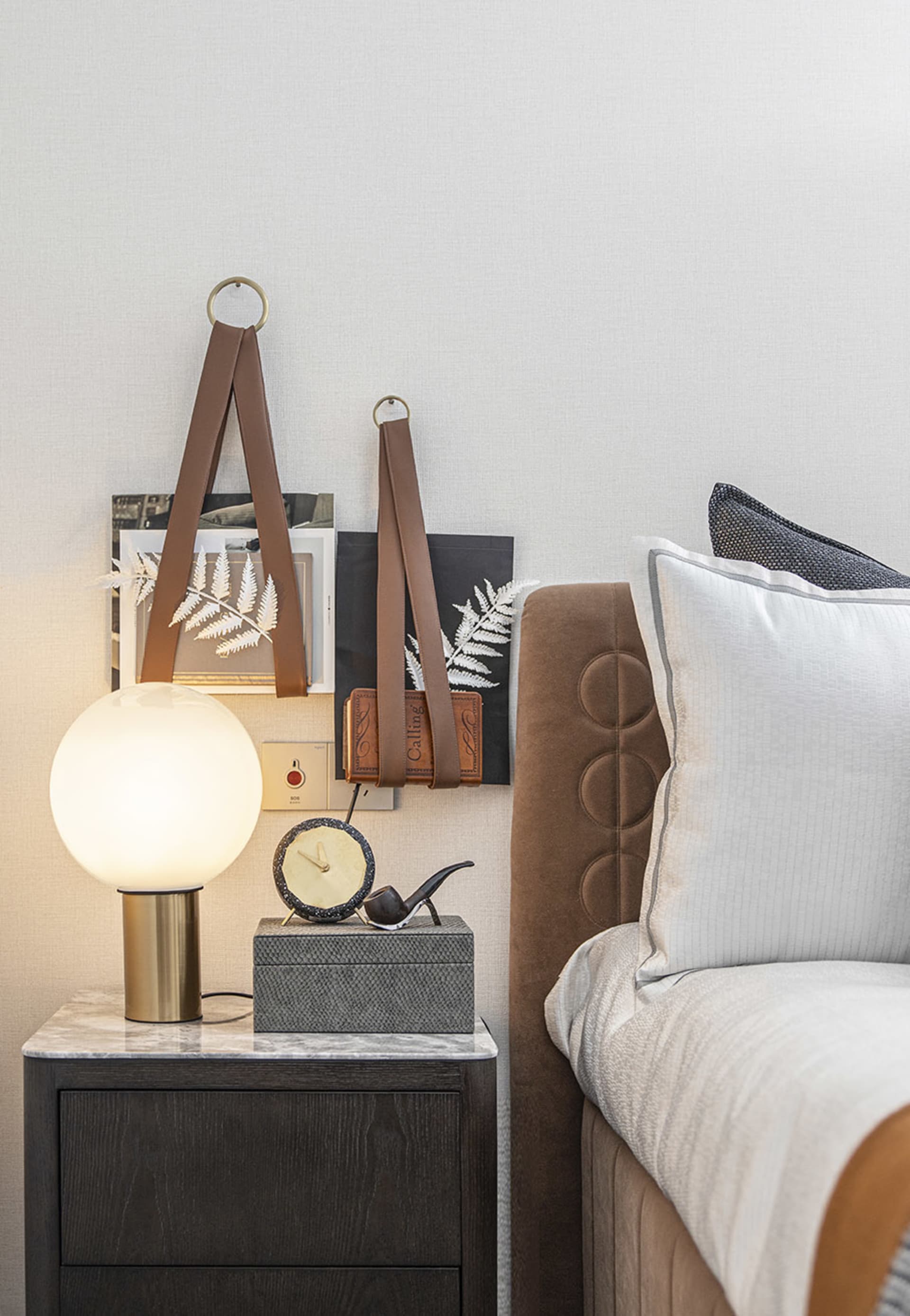 Modern bedroom with a brown upholstered bed, white and grey pillows, a nightstand with a spherical lamp, and decorative items
