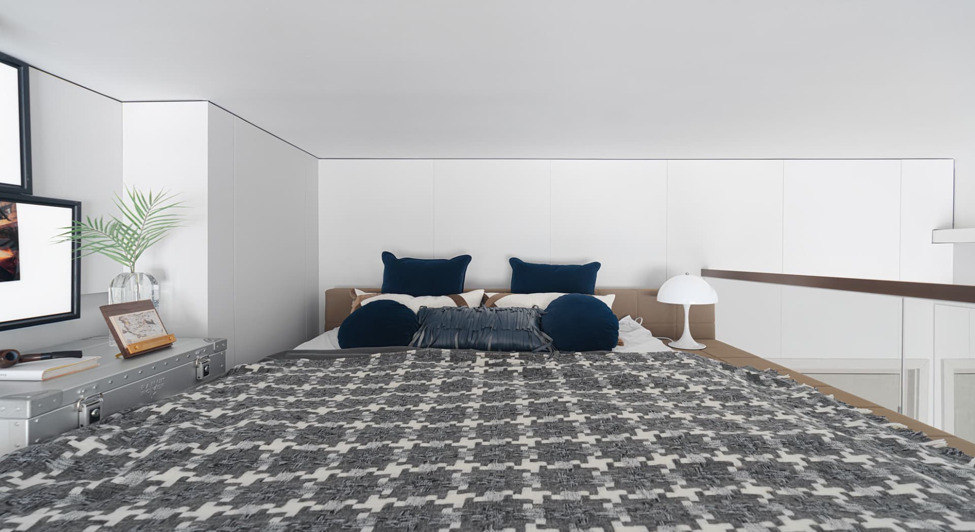 A modern bedroom featuring a bed with a variety of colorful textiles, including a gray and white patterned bedspread and blue