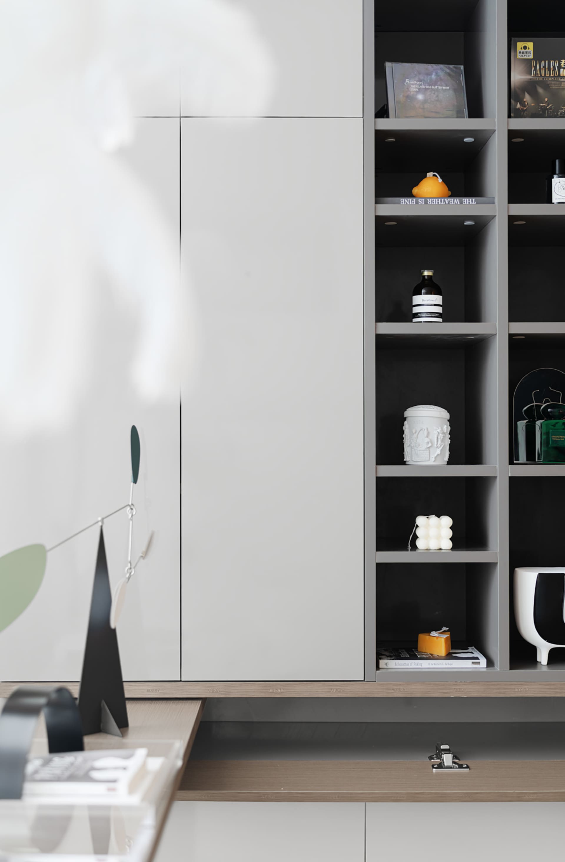 A modern living room with grey panels, glass windows, and several decorative items on shelves.