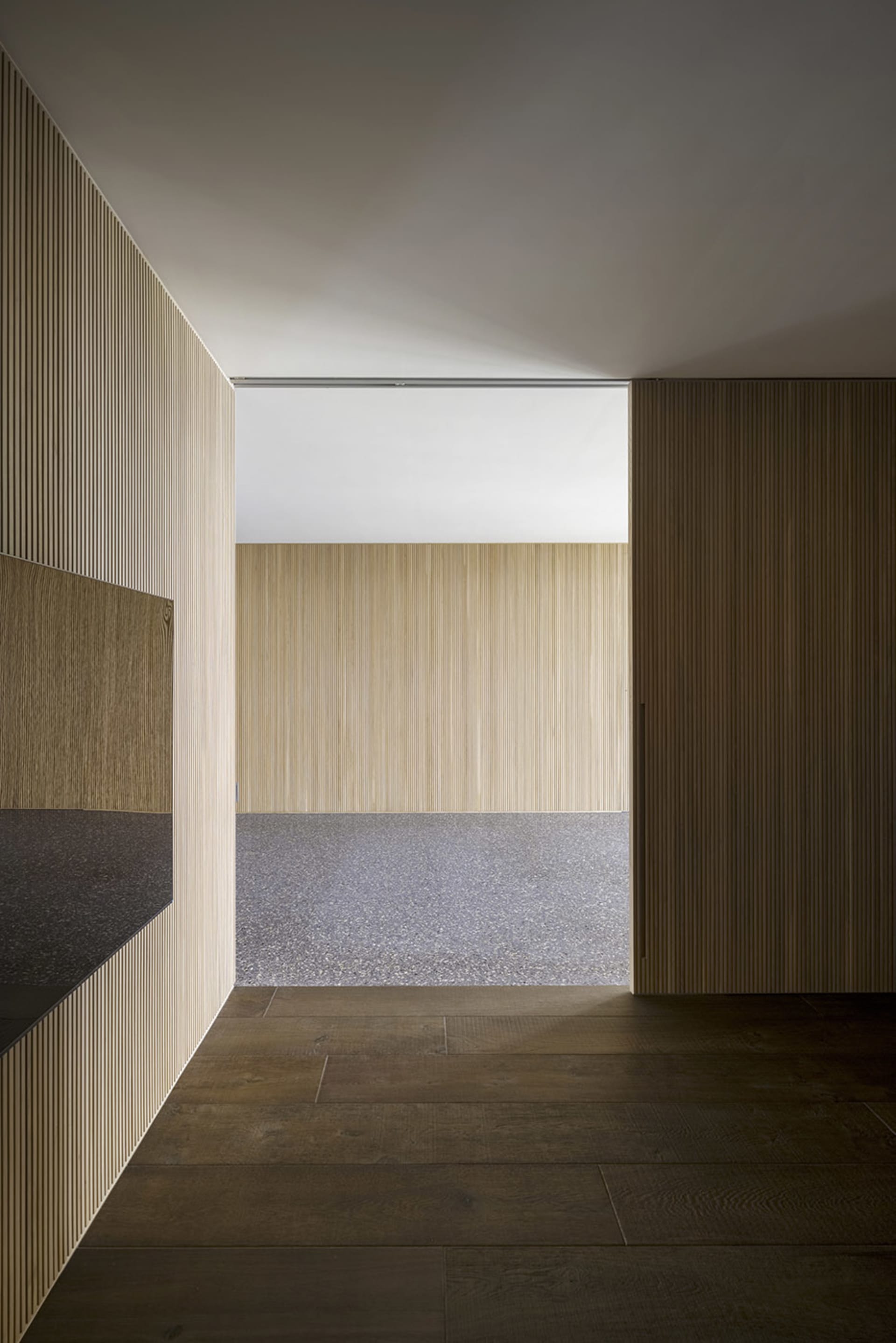 Modern interior design featuring a wooden slat entrance way with a contrasting textured floor.