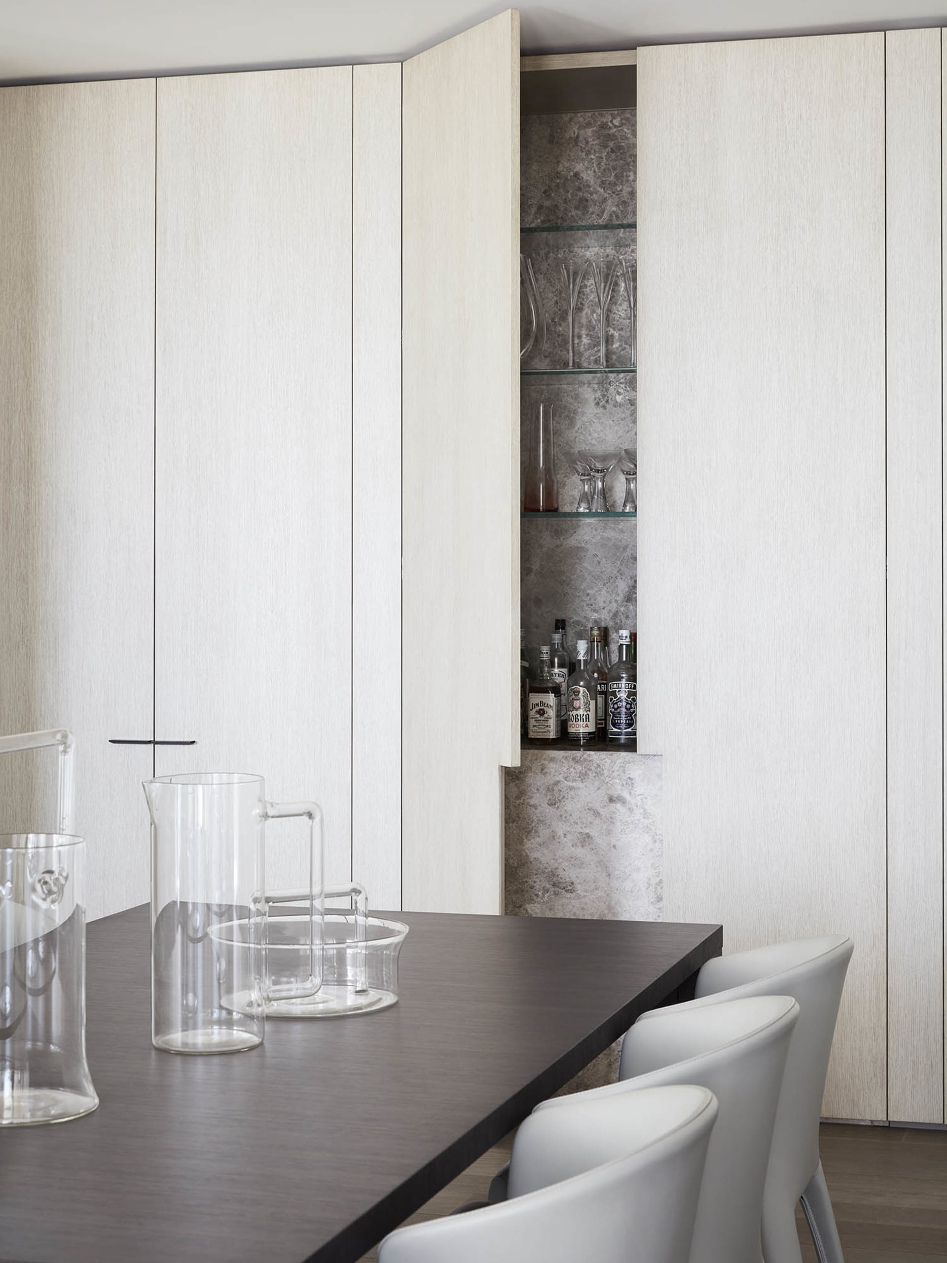 A modern kitchen with white storage cabinets, glassware, and bottles.