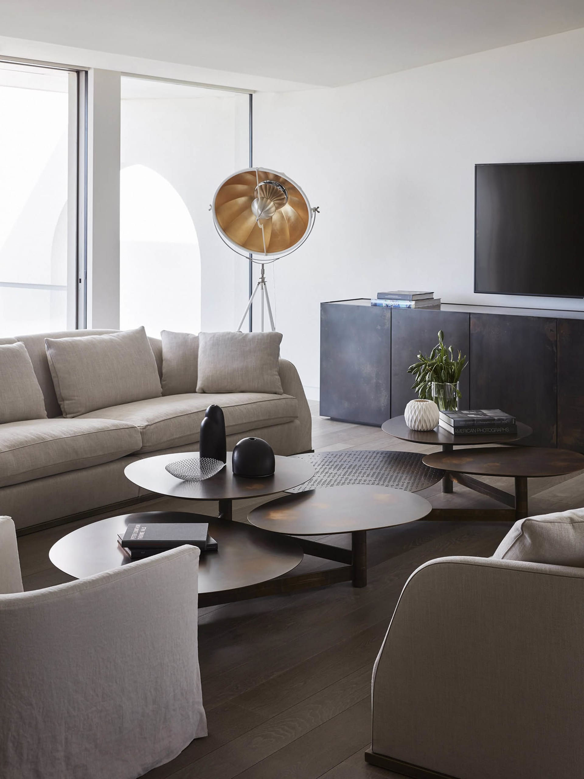 A modern living room featuring metal and wood furniture, minimalist design, and a floor lamp with a gold shade.