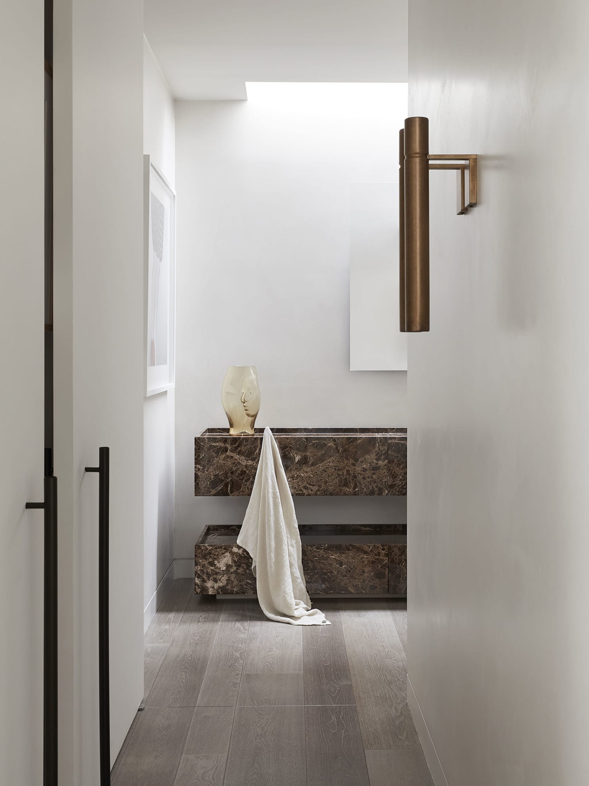A modern marble bathroom with a minimalist design featuring a vase on a counter and a towel draped over the edge.