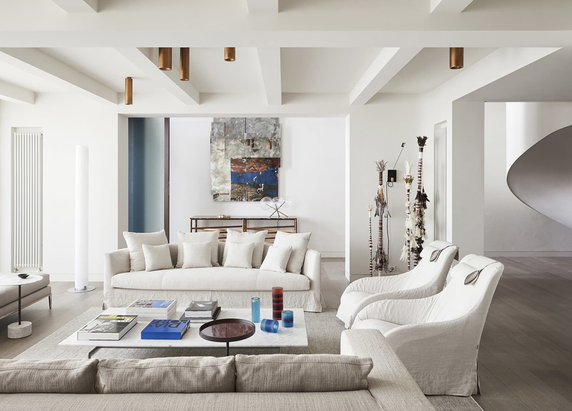 A modern white living room with a white sofa, armchairs, and coffee table with books and glass vases.