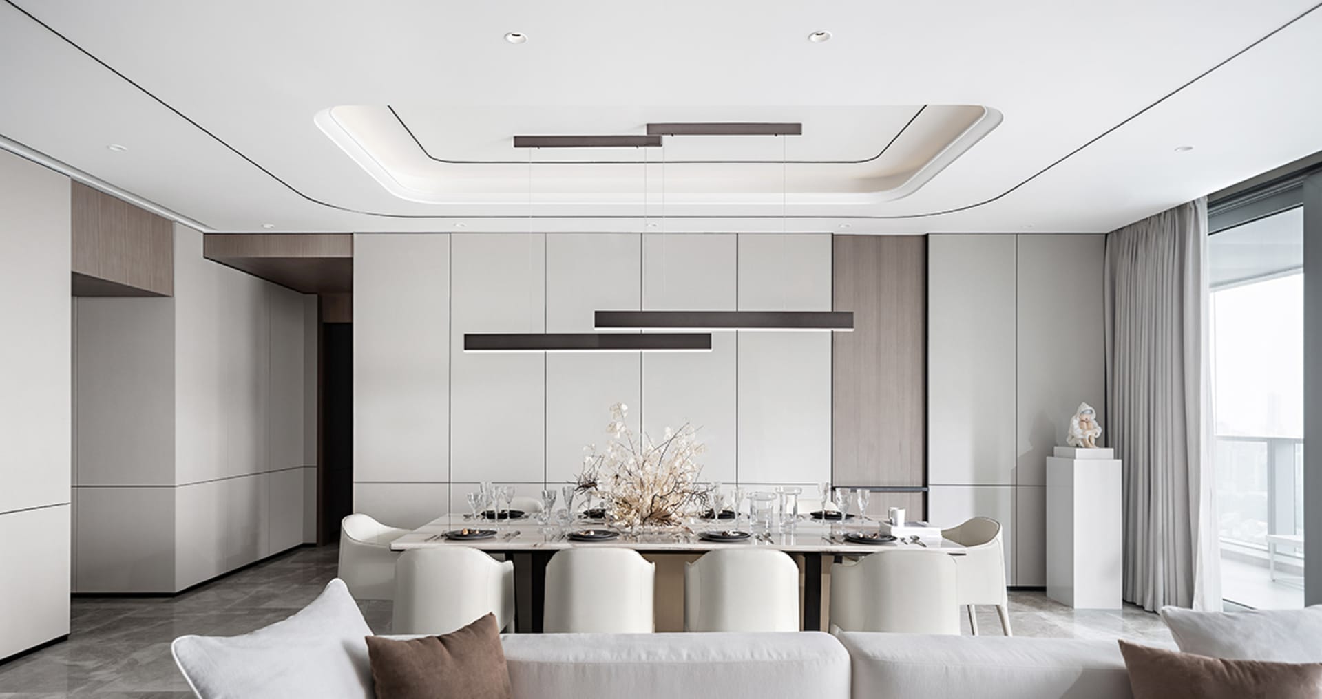 A modern dining room with a white concrete floor, white and grey walls, white pendant lights, and a long dining table.