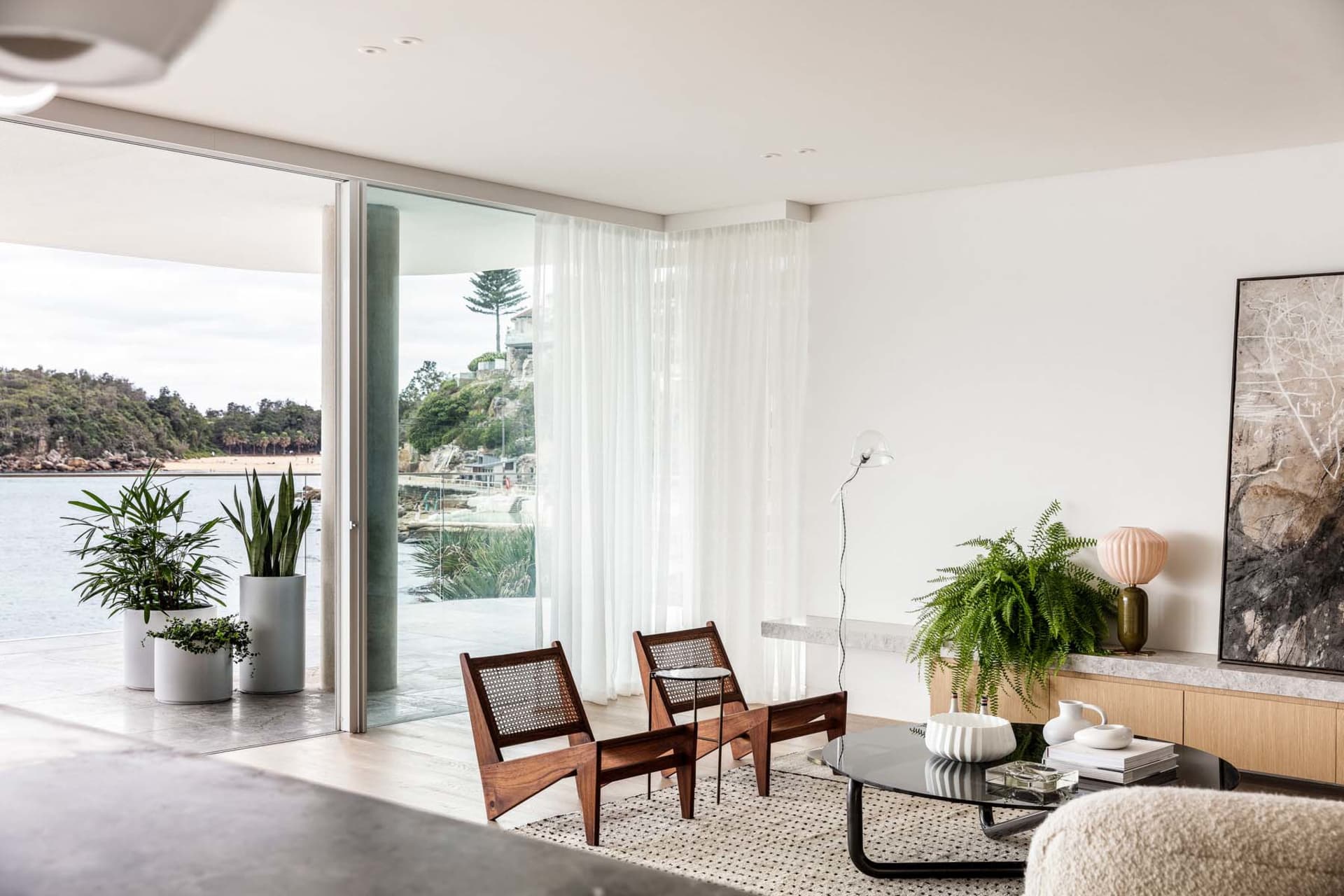 Modern minimalist living room with wood accents, white sheer curtains, and a view of a serene outdoor area.