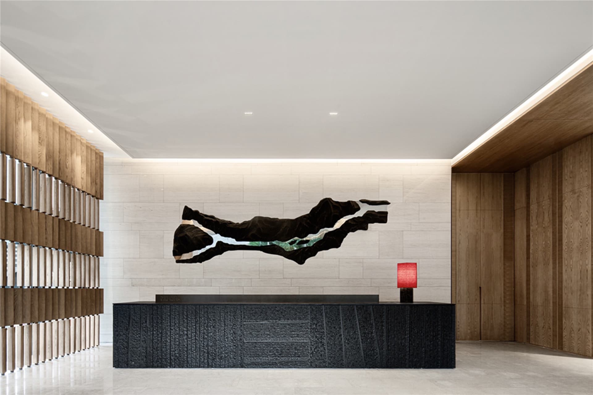 A modern entry way featuring a black wooden desk, a red lamp, and a large abstract black and white sculpture on a white and b