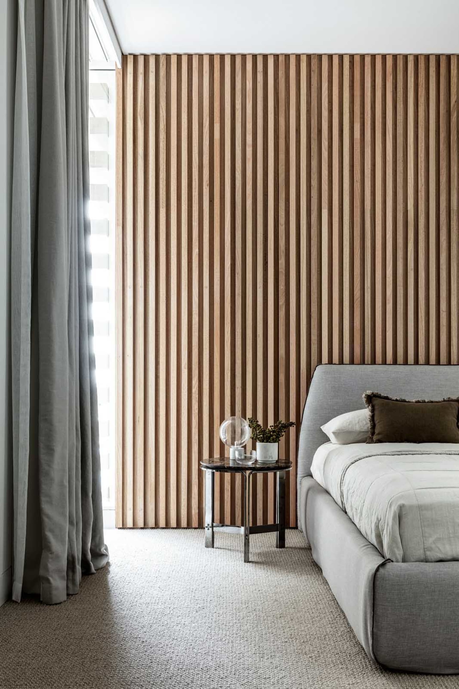 Modern minimalist bedroom featuring a grey upholstered bed with wooden slat paneling on the wall.