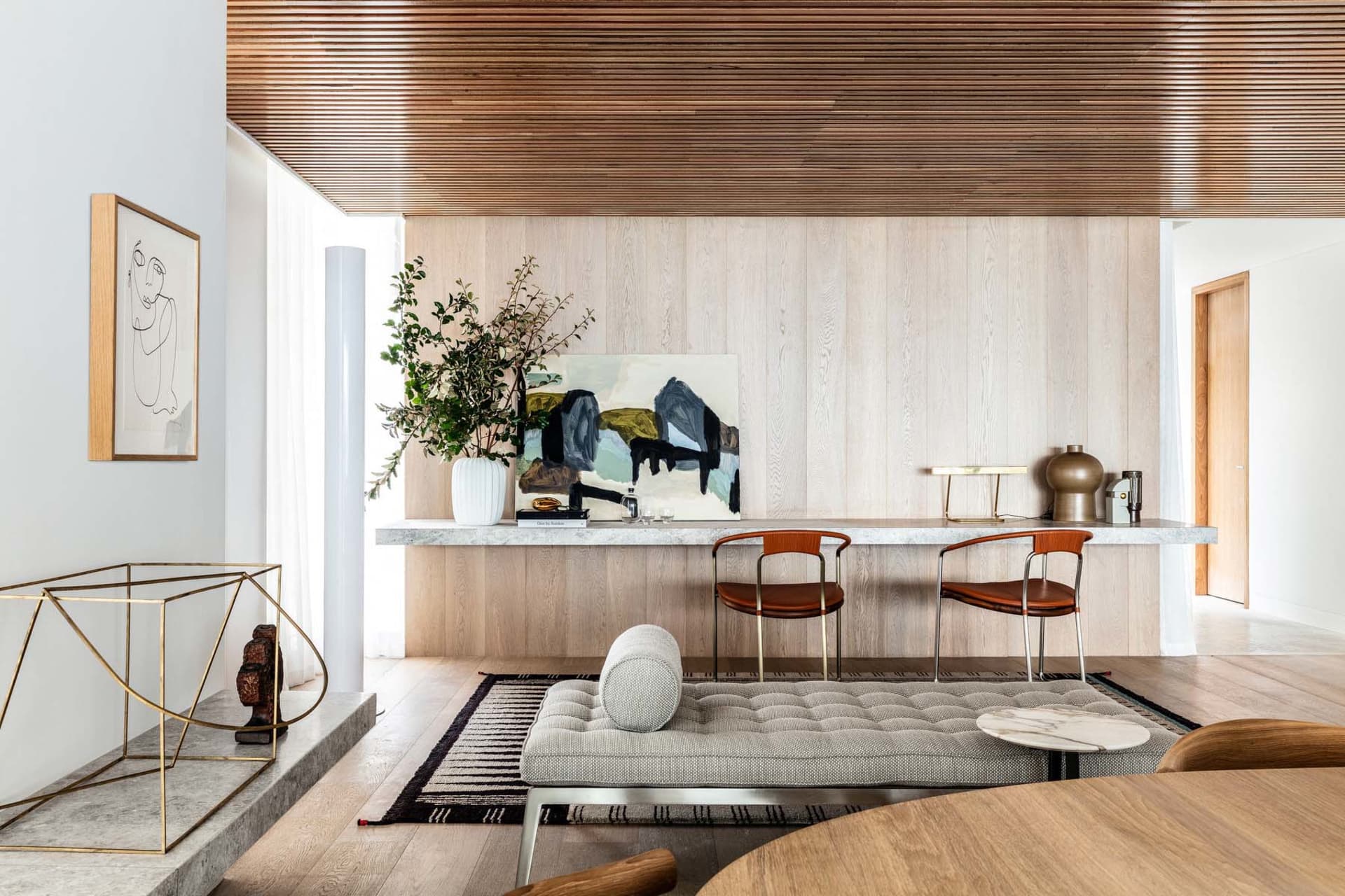 A contemporary living room featuring marble and wooden furniture, with a minimalist design and abstract artwork.