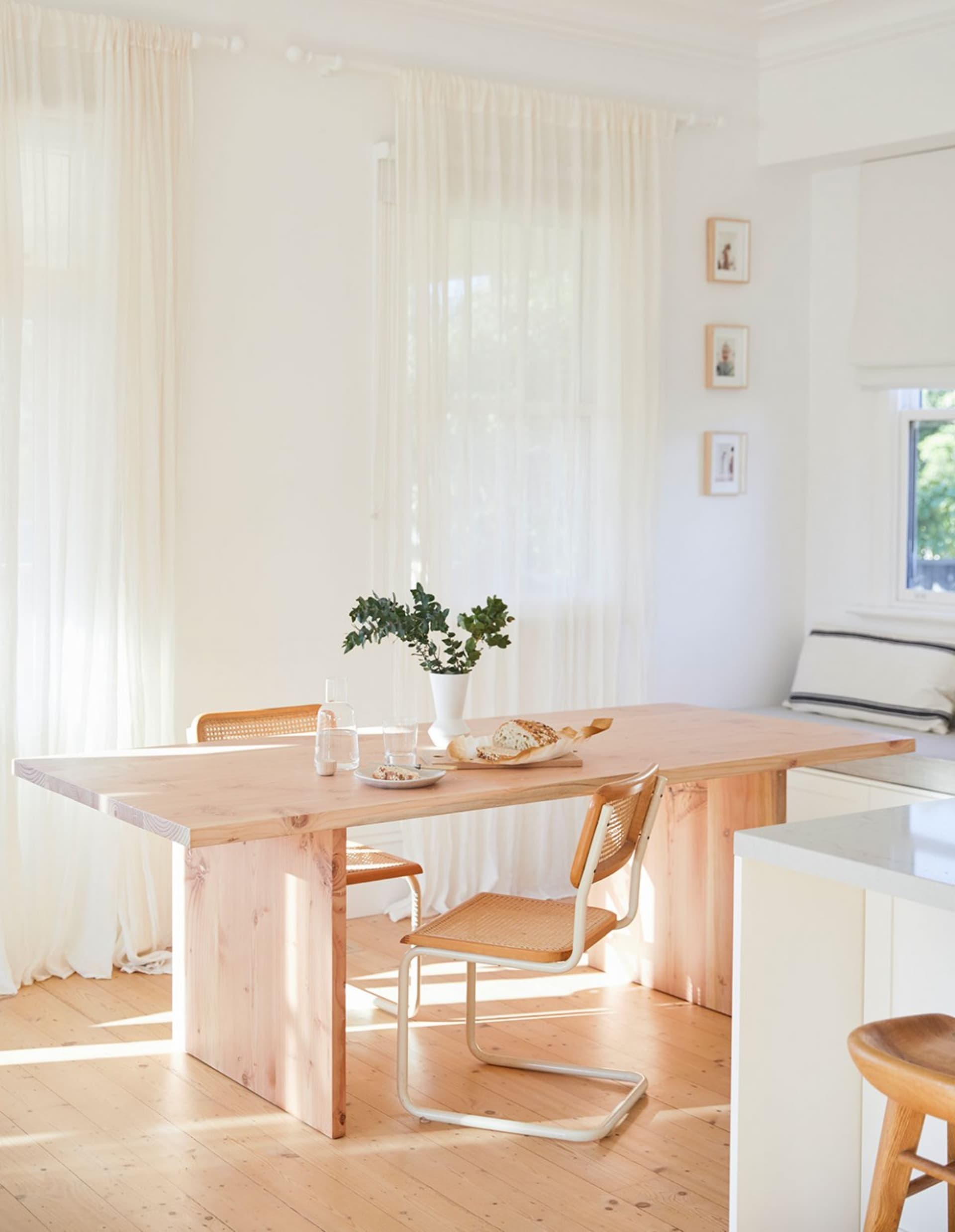 A minimalist kitchen with wooden elements, including a table and chairs, a vase with greenery, and a bread loaf.