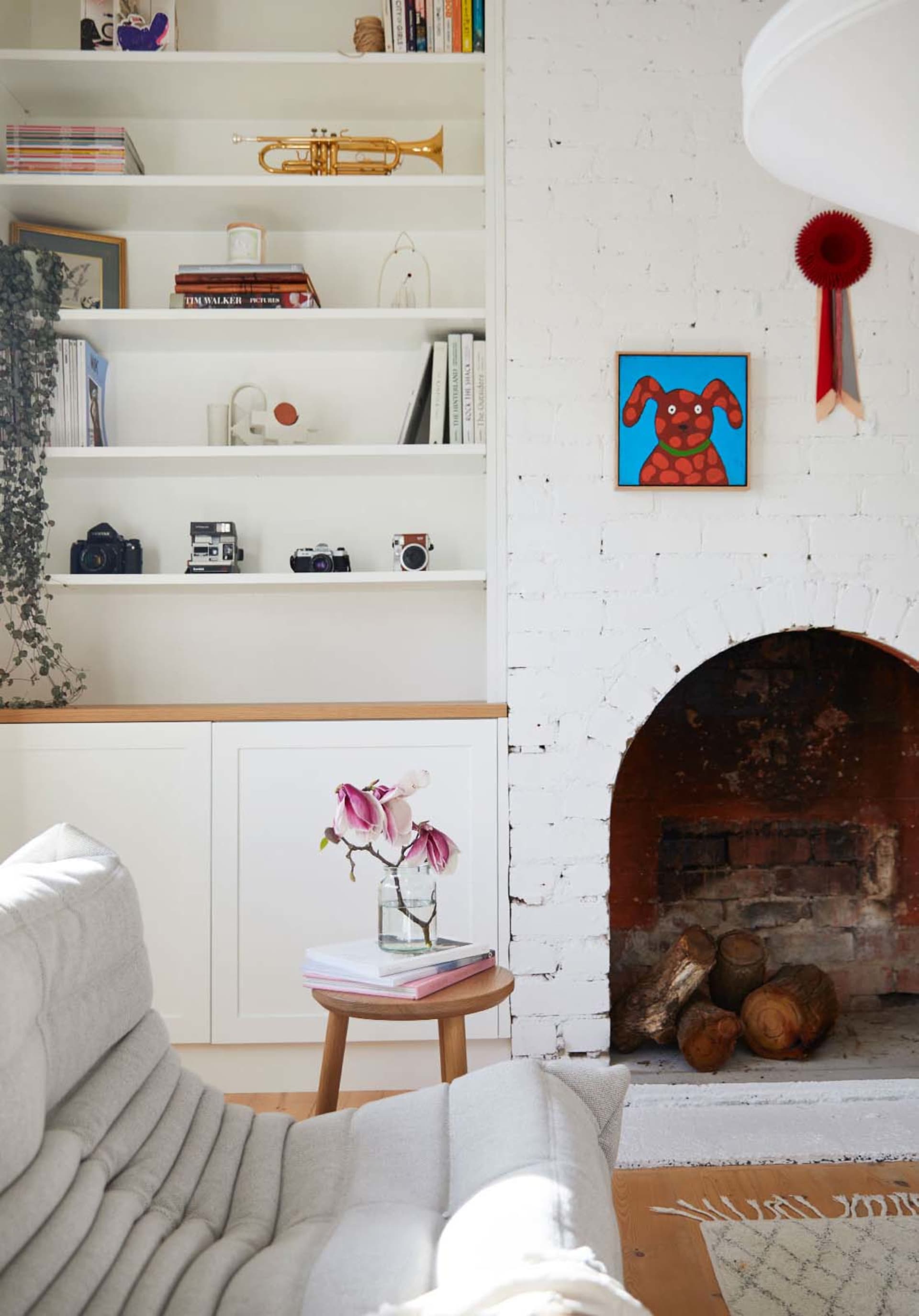 A minimalist living room with a white couch, wooden coffee table, and a white brick fireplace.